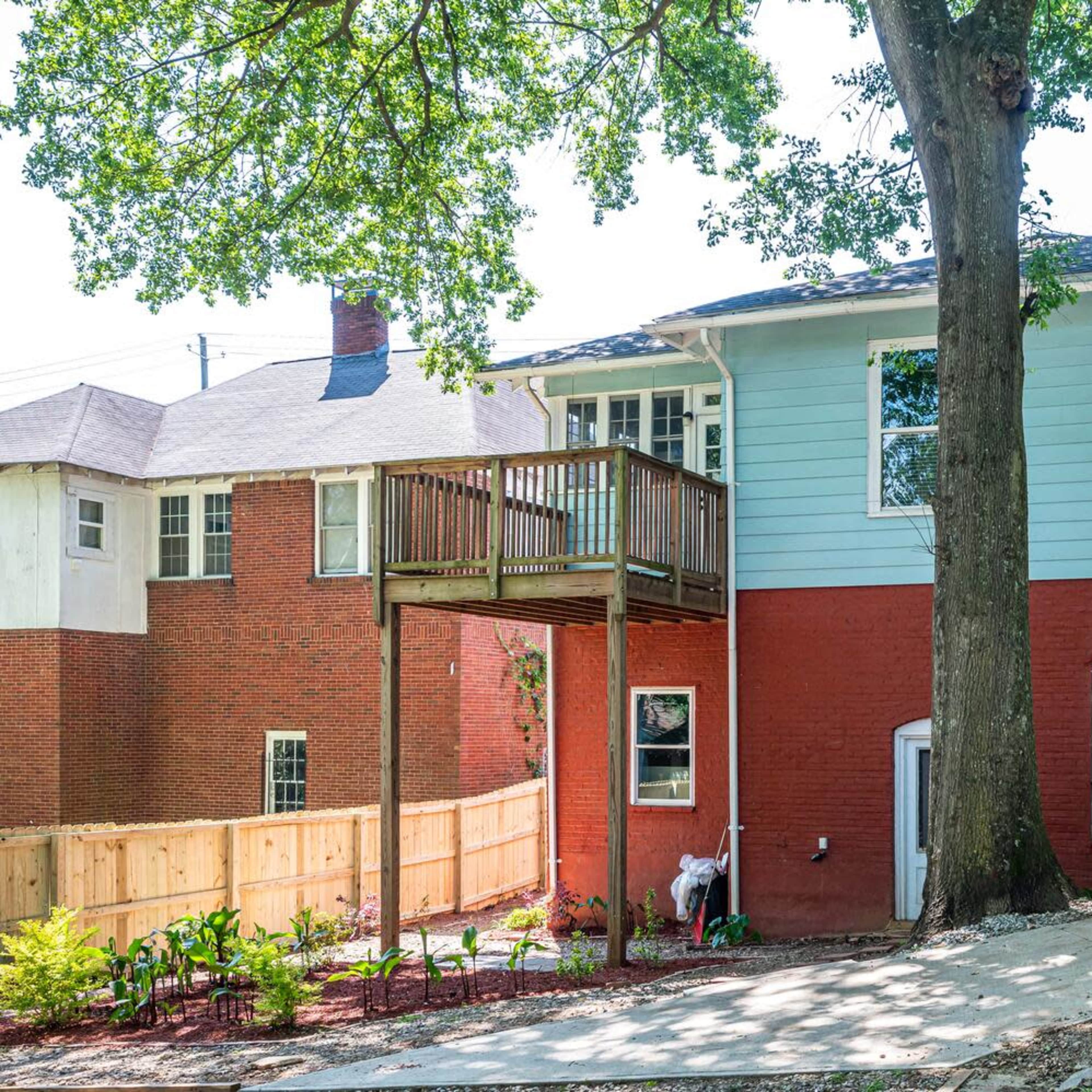 A two-story house with a deck, located beside a yard with landscaping and a protective fence.