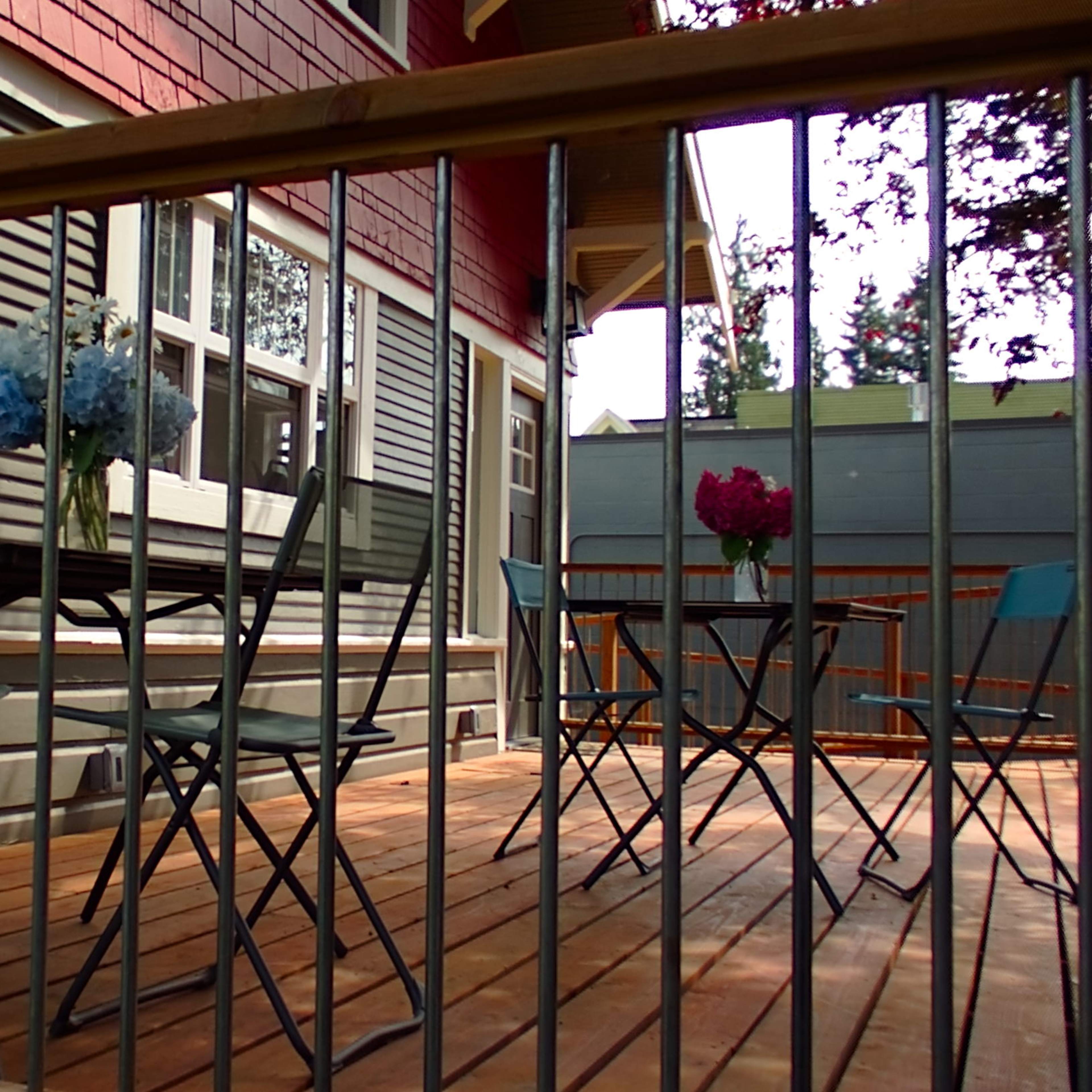 A wooden deck features two tables with vases of flowers and is surrounded by a railing.
