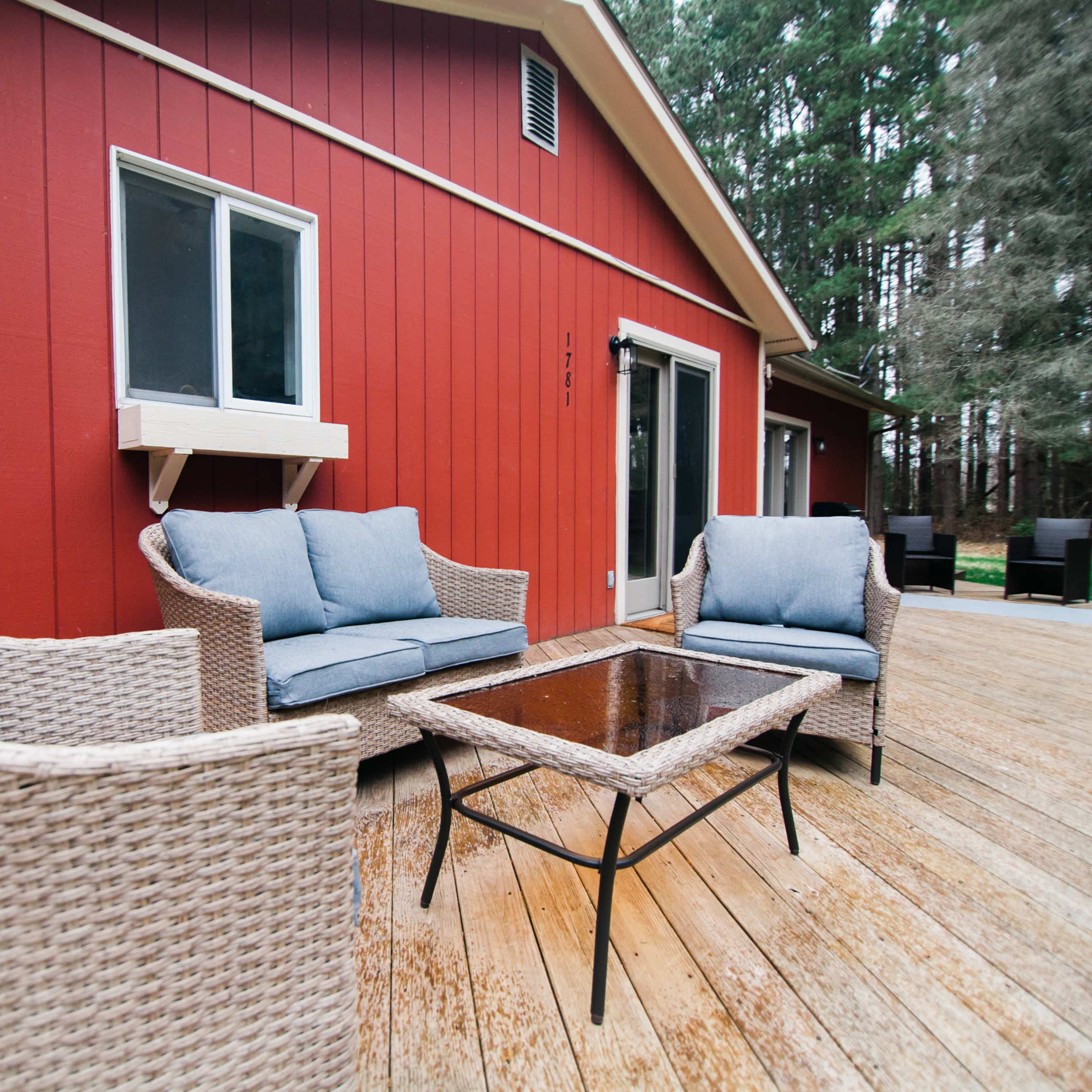 A red house with a wooden deck features two wicker chairs and a glass-top coffee table.