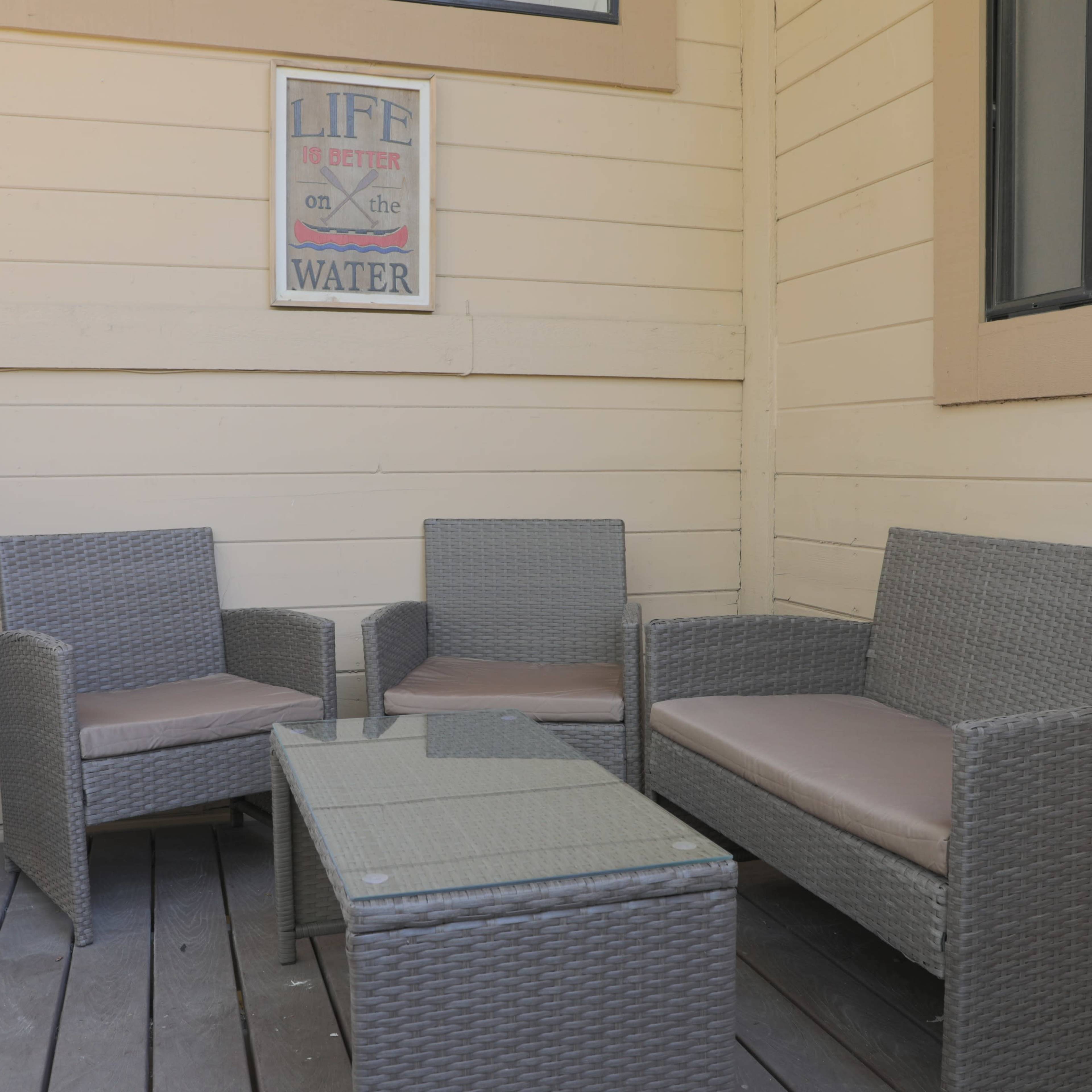 A covered porch features four pieces of wicker furniture: two armchairs, a loveseat, and a coffee table.