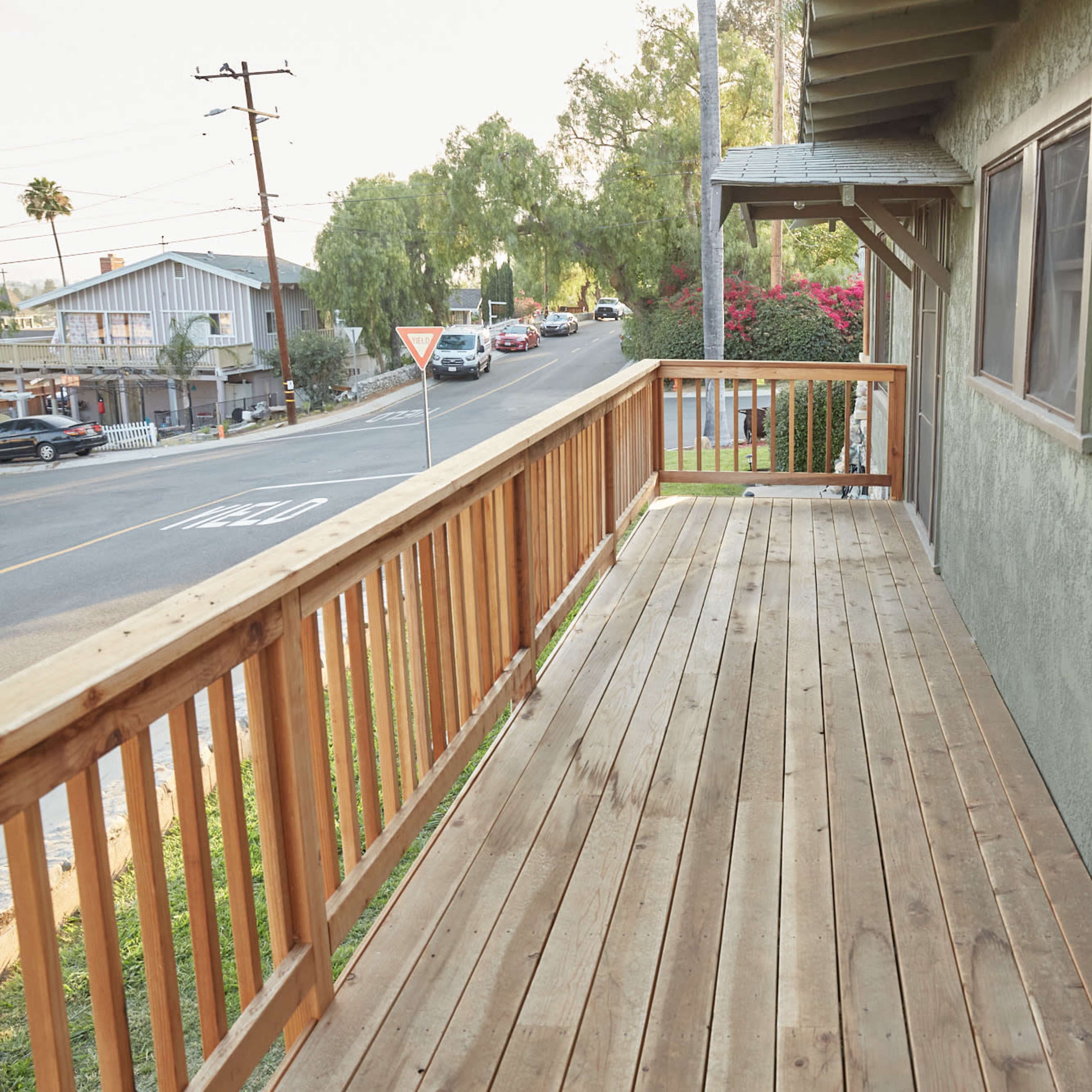 A wooden deck lines the exterior of a building, with a view of a road and nearby houses.