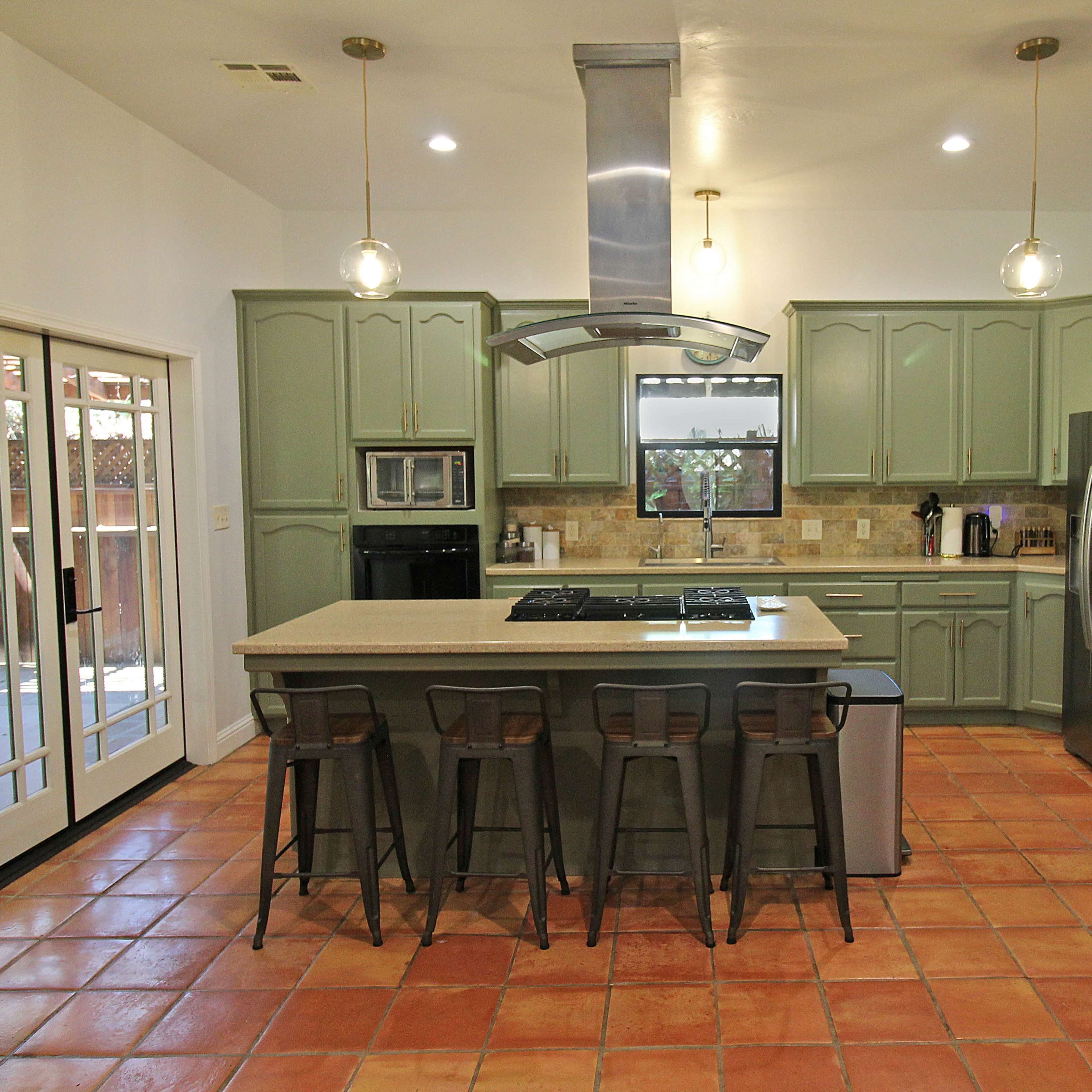A spacious kitchen with green cabinetry, a large island with bar stools, and a window overlooking an outdoor area.