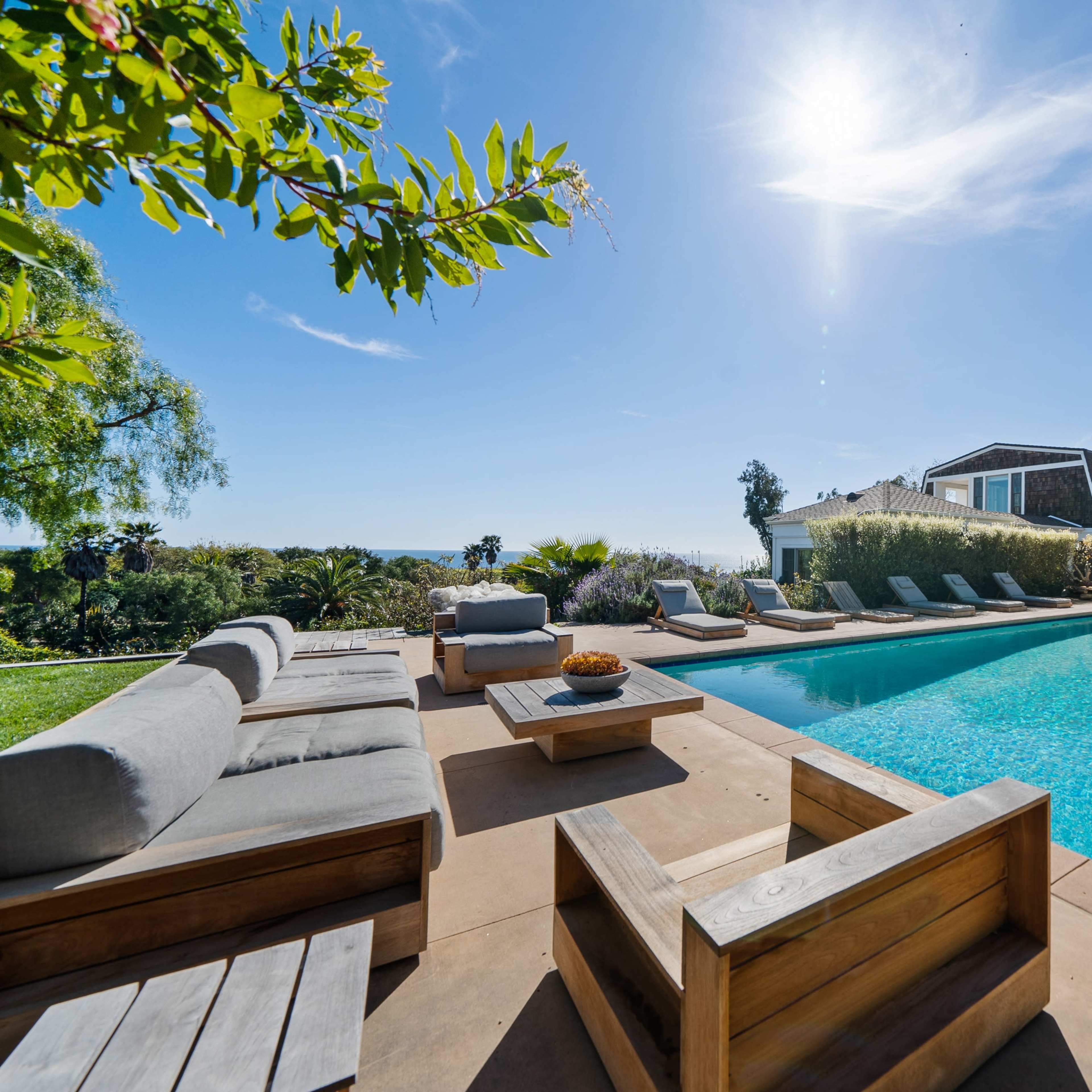 A modern outdoor area features a swimming pool surrounded by lounge chairs and wooden seating against a clear sky.