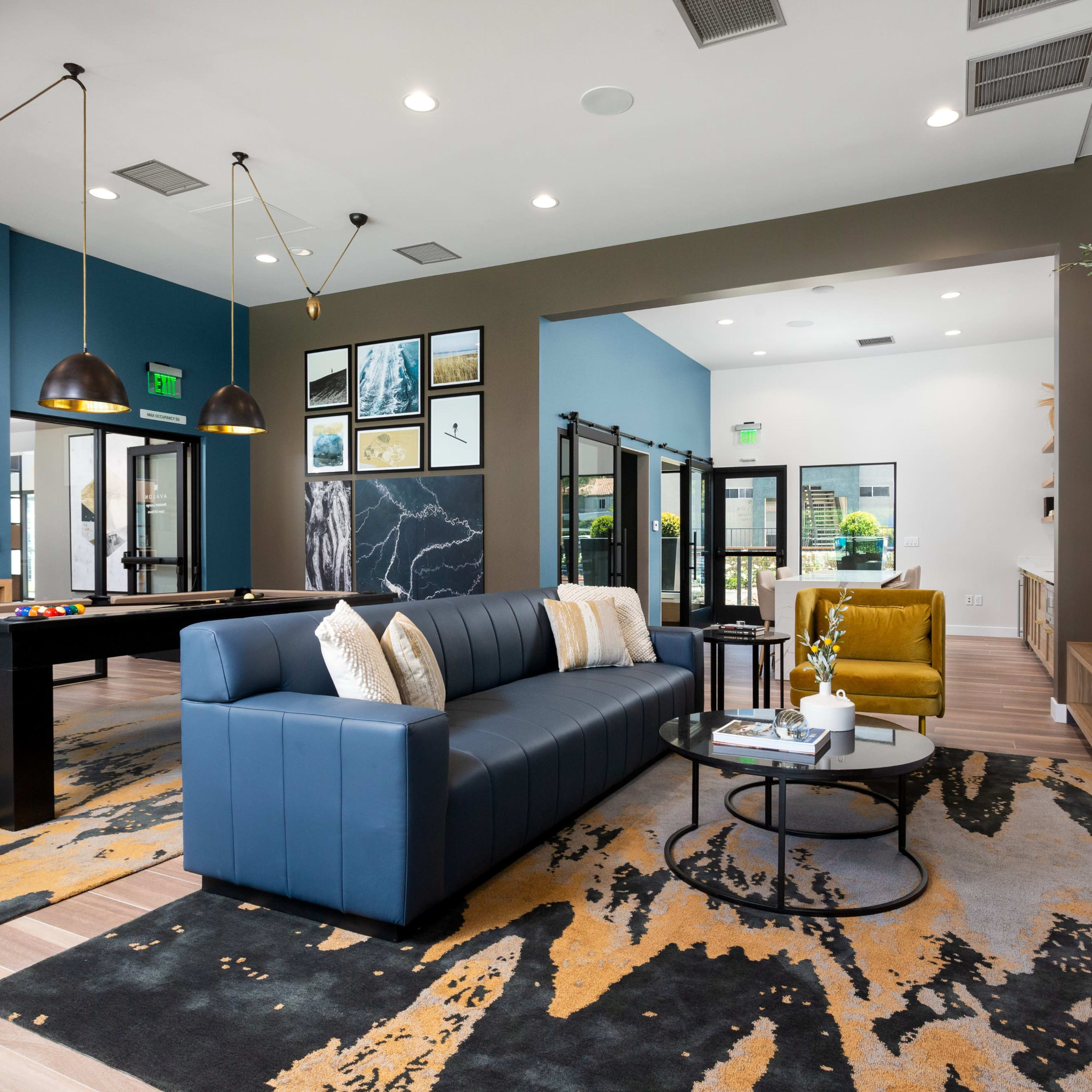 A modern lounge area with a blue sofa, a pool table, and a large television mounted on the wall, surrounded by decorative artwork and plants.
