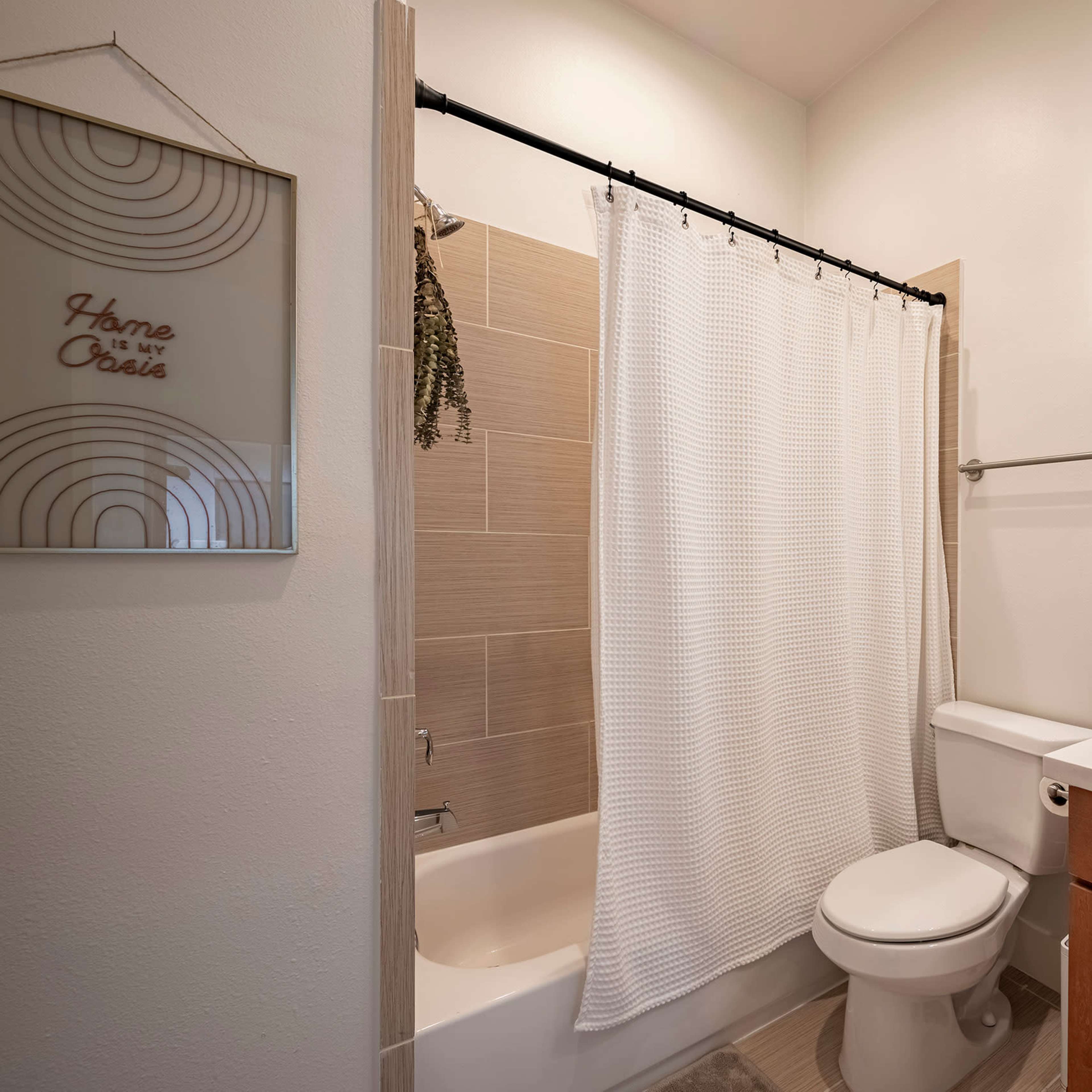 The bathroom features a bathtub with a shower curtain, a modern vanity with a sink, and neutral-toned tiles on the walls.