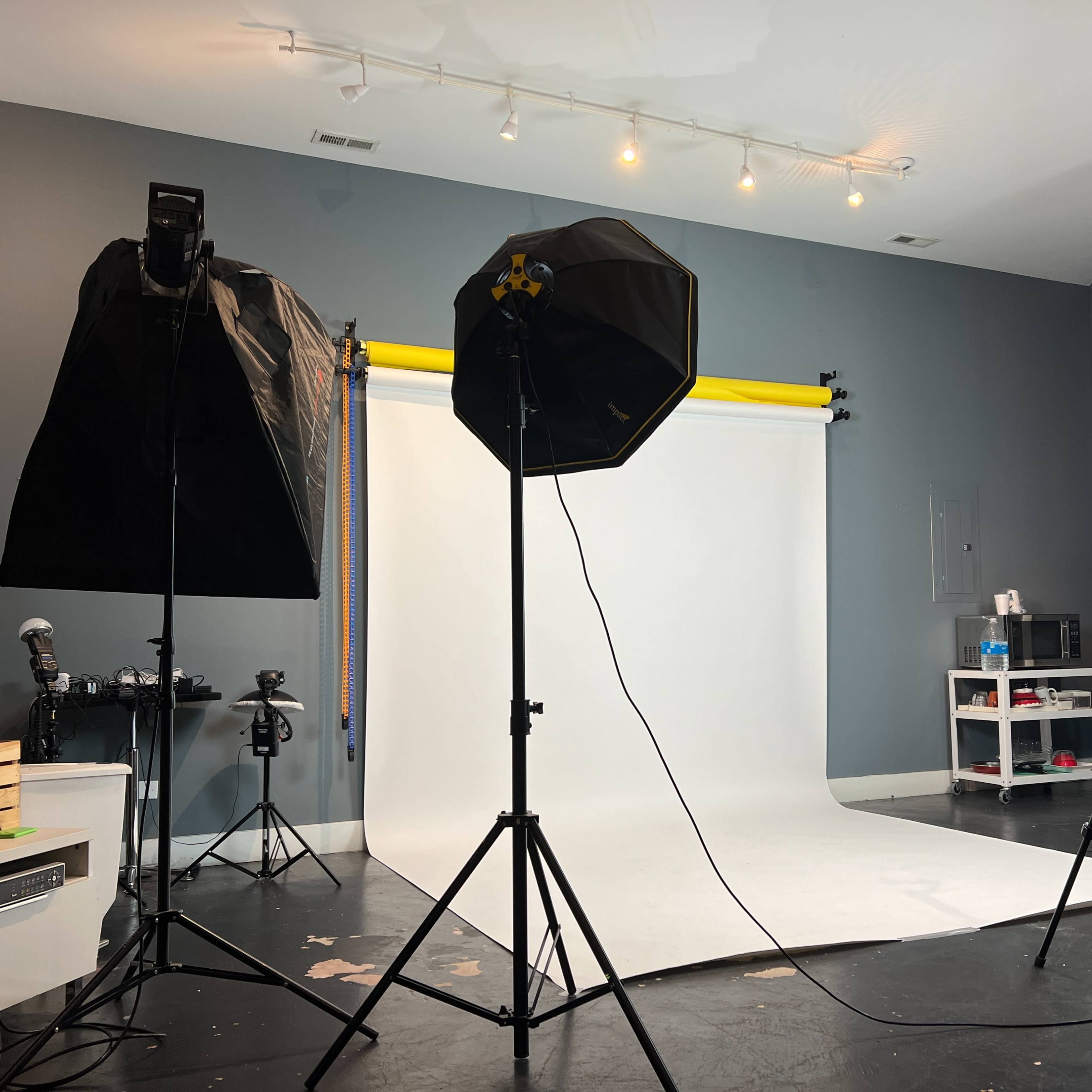 A photography studio is set up with softbox lighting on either side and a white backdrop in the center.