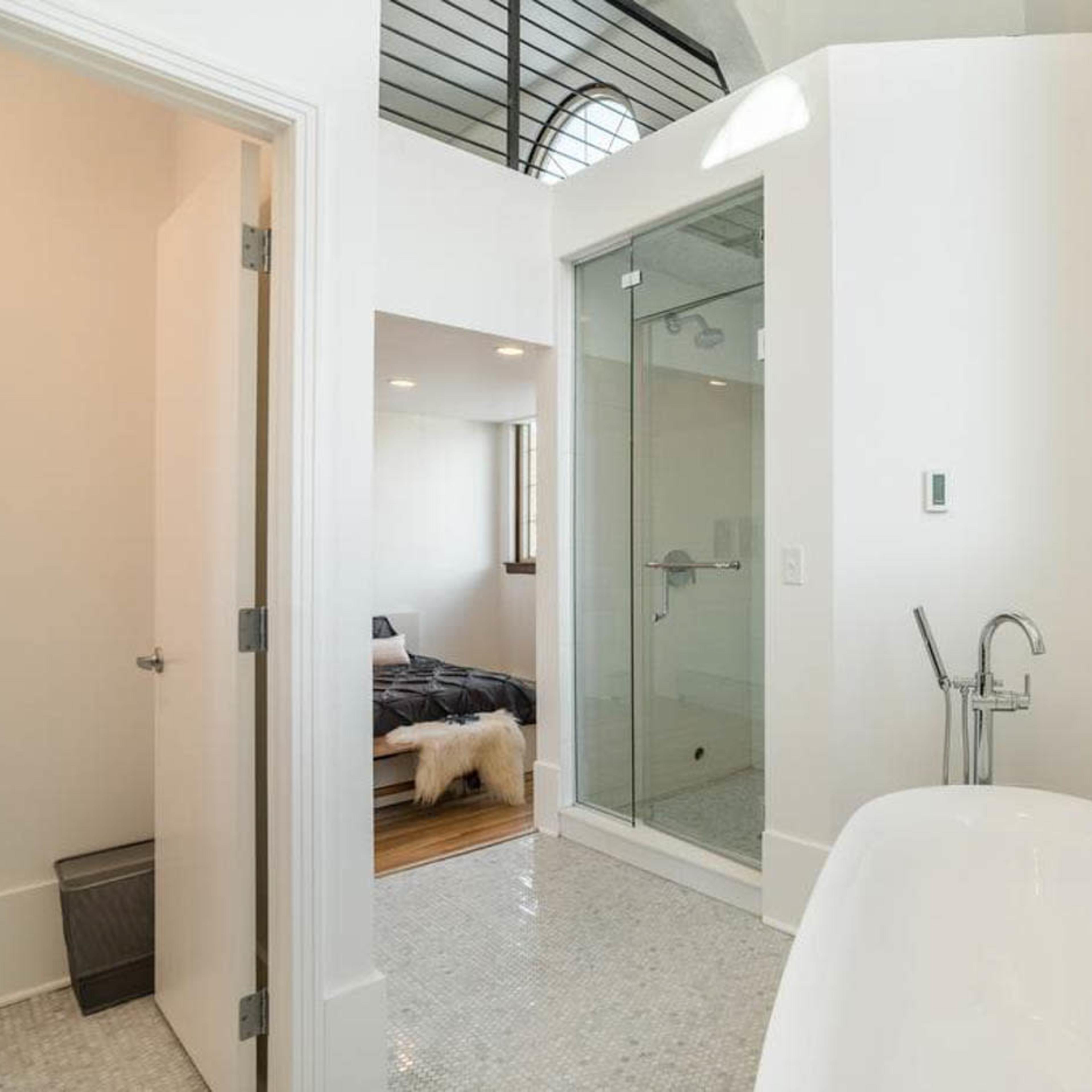 A clean, modern bathroom featuring a freestanding bathtub and a shower enclosure, with a glimpse of a bedroom in the background.
