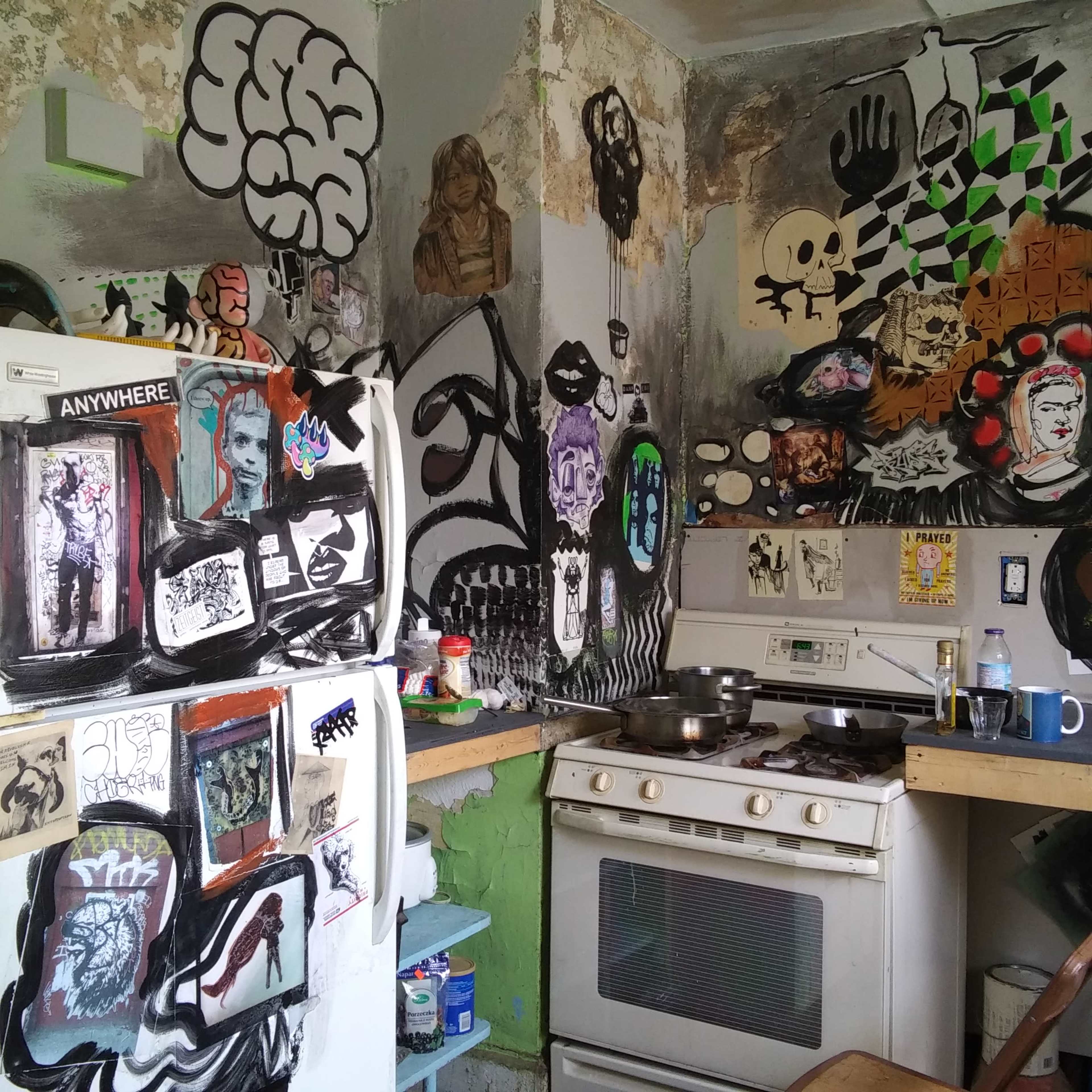 A cluttered kitchen with graffiti-style art covering the walls and appliances.