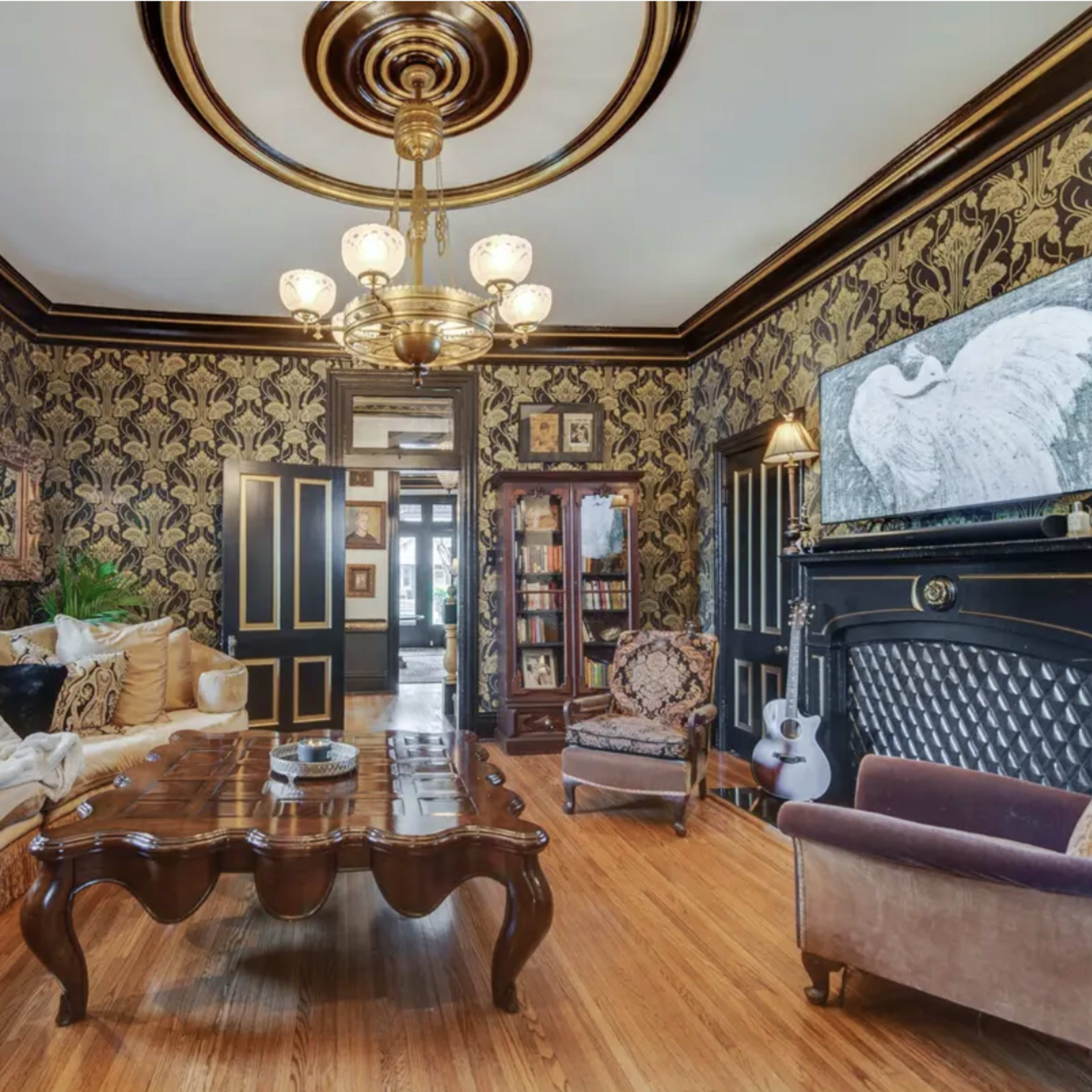 The room features ornate wallpaper, a vintage chandelier, and a mix of seating arrangements around a dark wood coffee table.