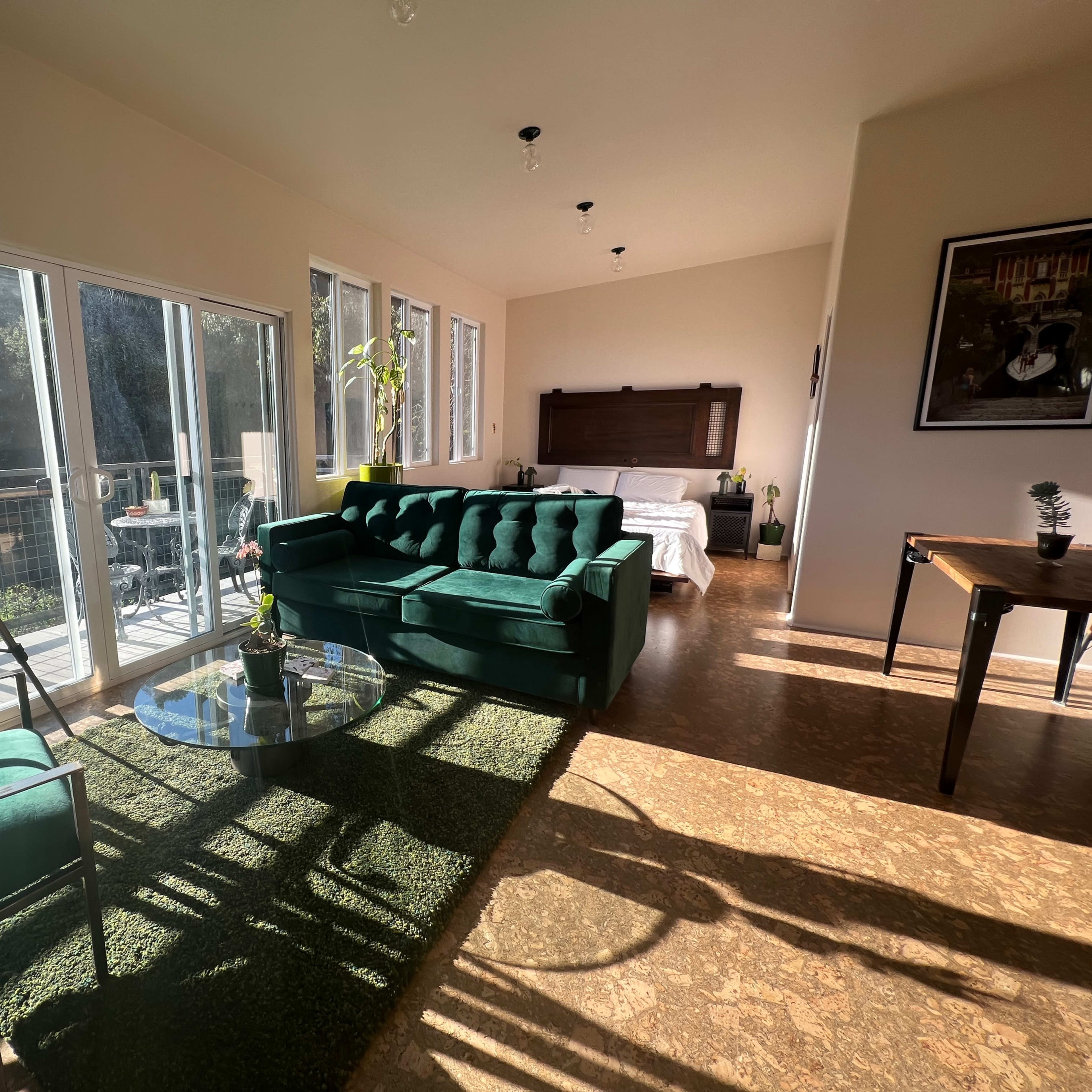 The interior features a green velvet sofa, a glass coffee table, and large windows that flood the space with natural light.