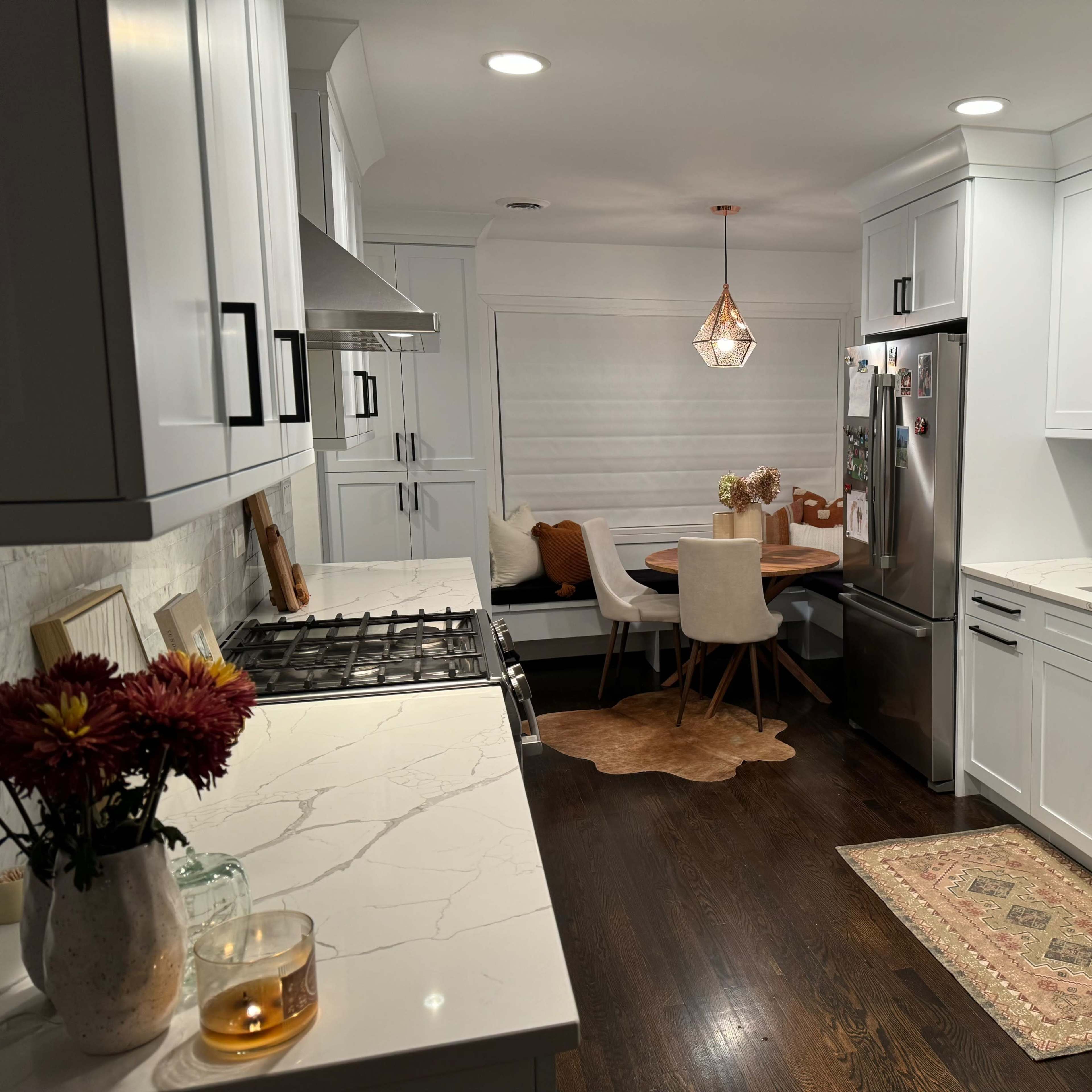 A modern kitchen with white cabinets, a marble countertop, a stainless steel refrigerator, and a dining area featuring a round table and plush seating.