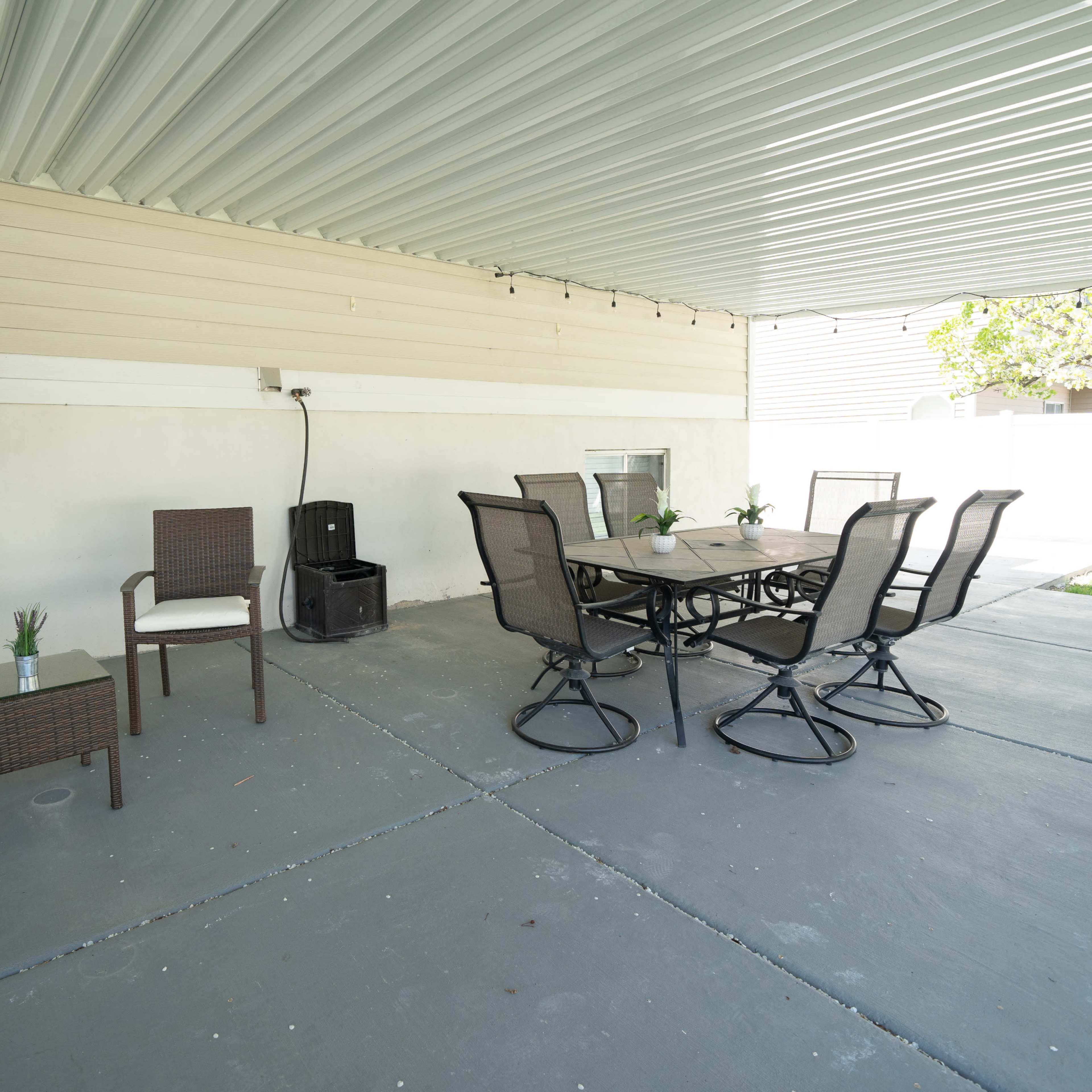 A covered patio area with a table and six chairs, along with two additional chairs on one side.