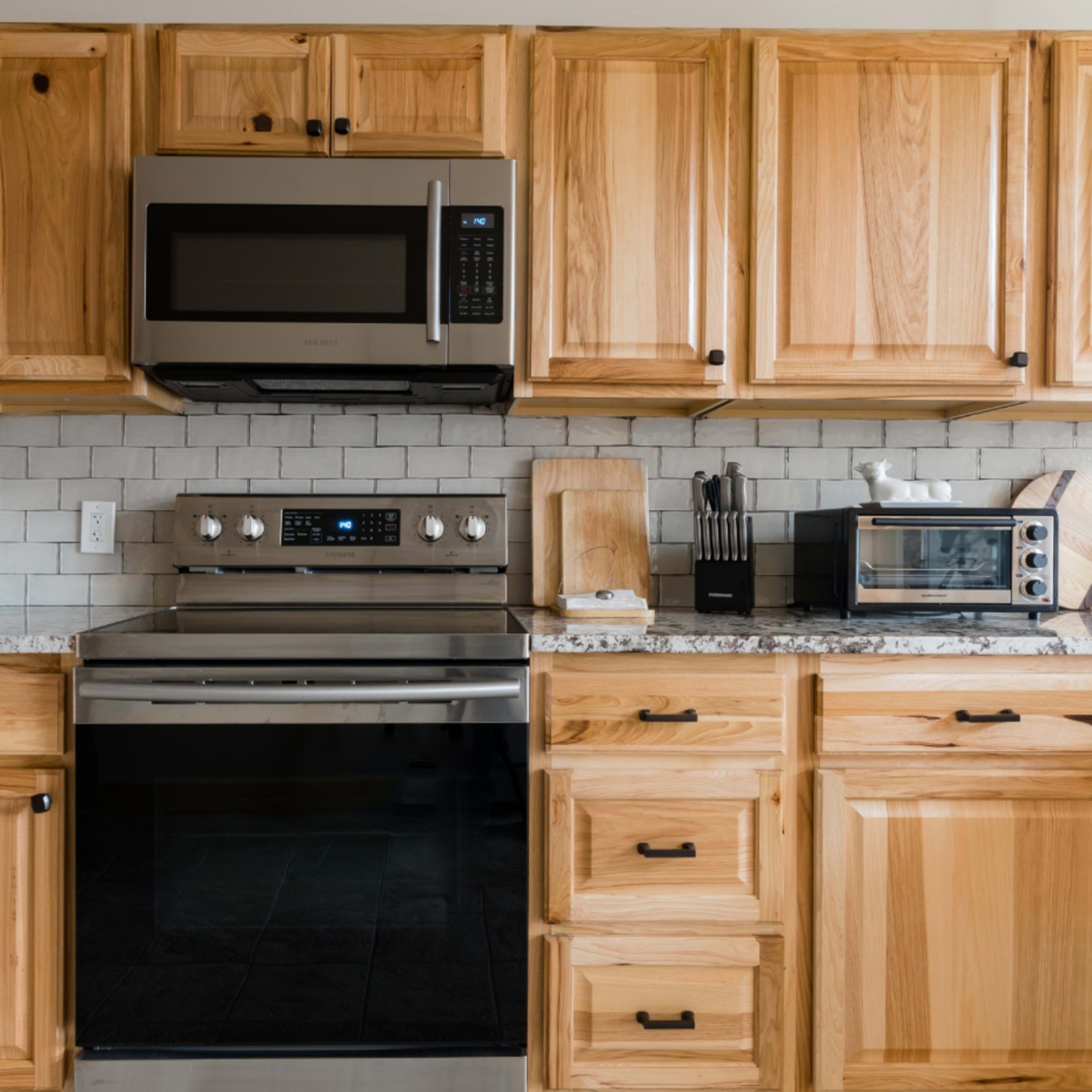A modern kitchen with wooden cabinets, a stainless steel microwave, and an oven set against a tiled backsplash.