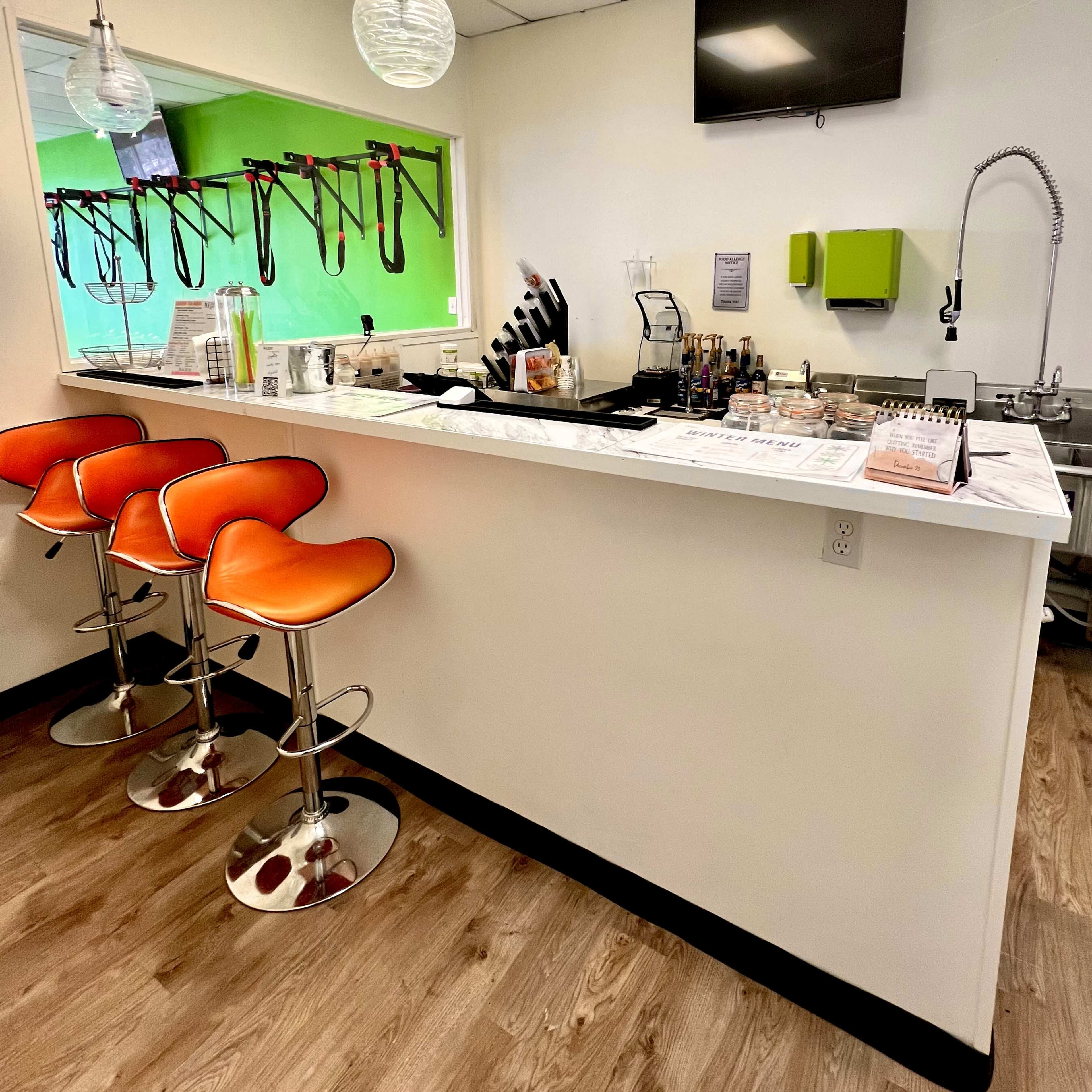 A modern bar counter with orange stools, a selection of kitchen utensils, and a sink in a brightly lit, open space.