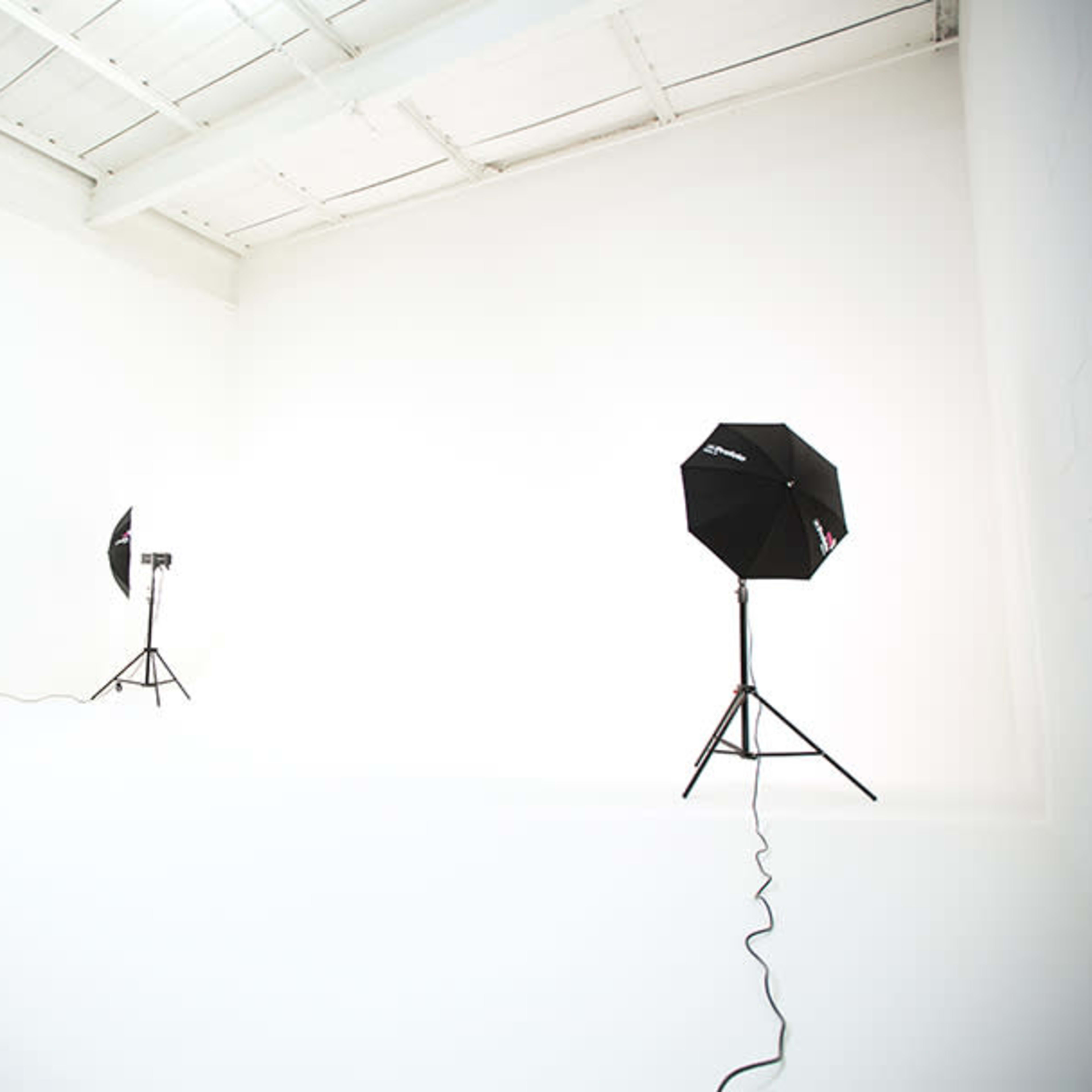 An empty photography studio with two light stands and a seamless white backdrop.