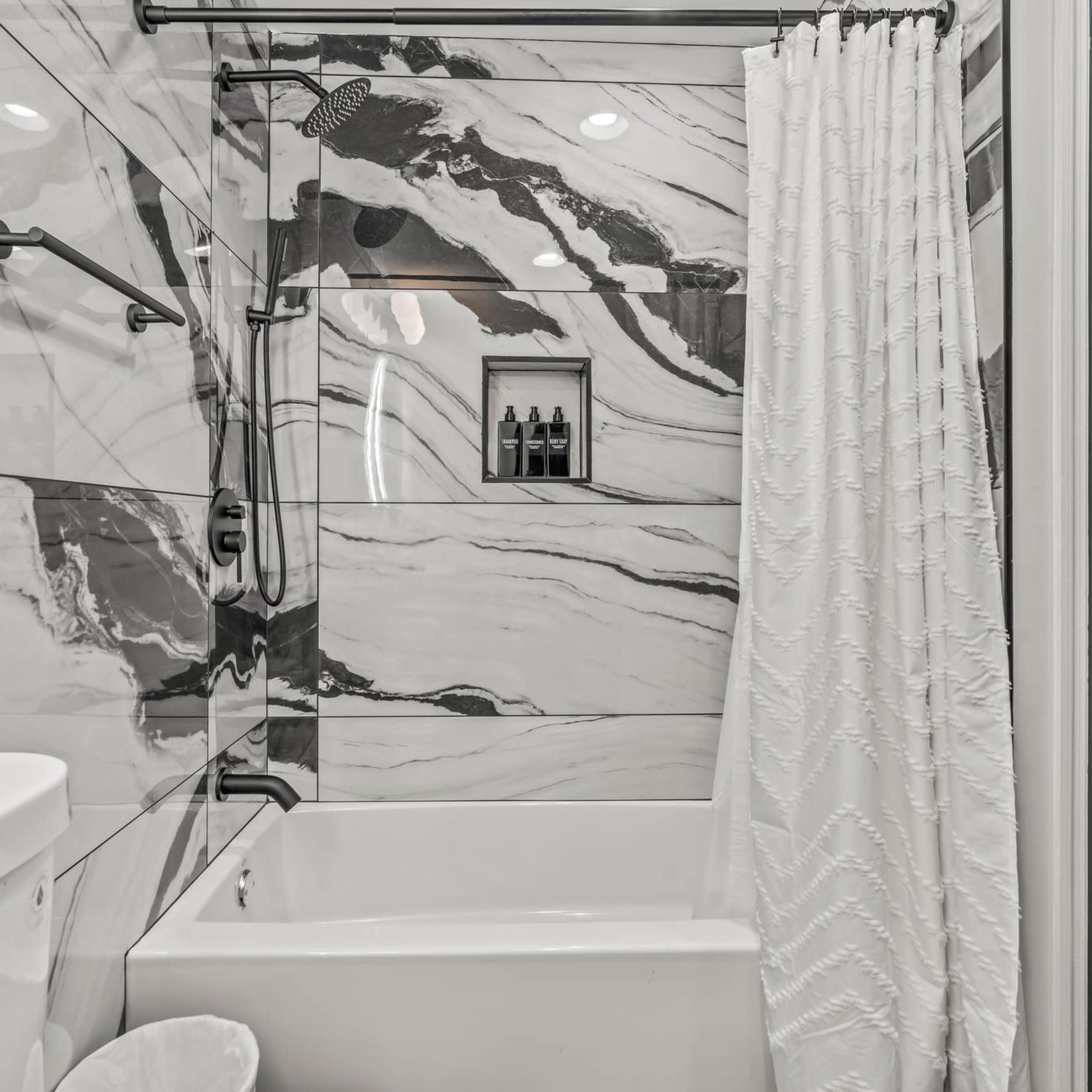 A bathroom featuring a tub and shower combination with marble-patterned tiles and a white curtain.