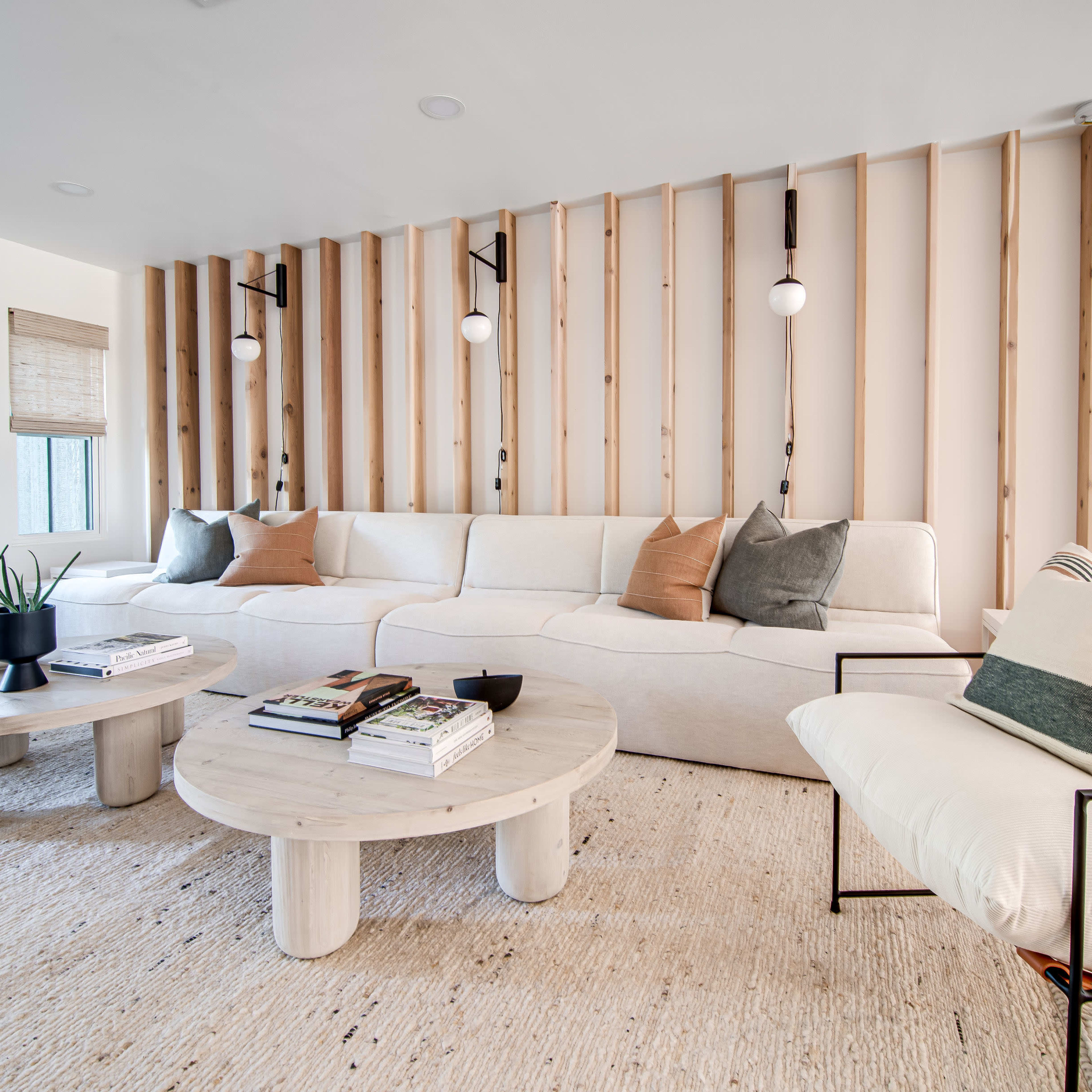 A modern living room with a sectional sofa, a round coffee table, and two accent chairs, all arranged around a textured rug against a backdrop of wooden wall slats.