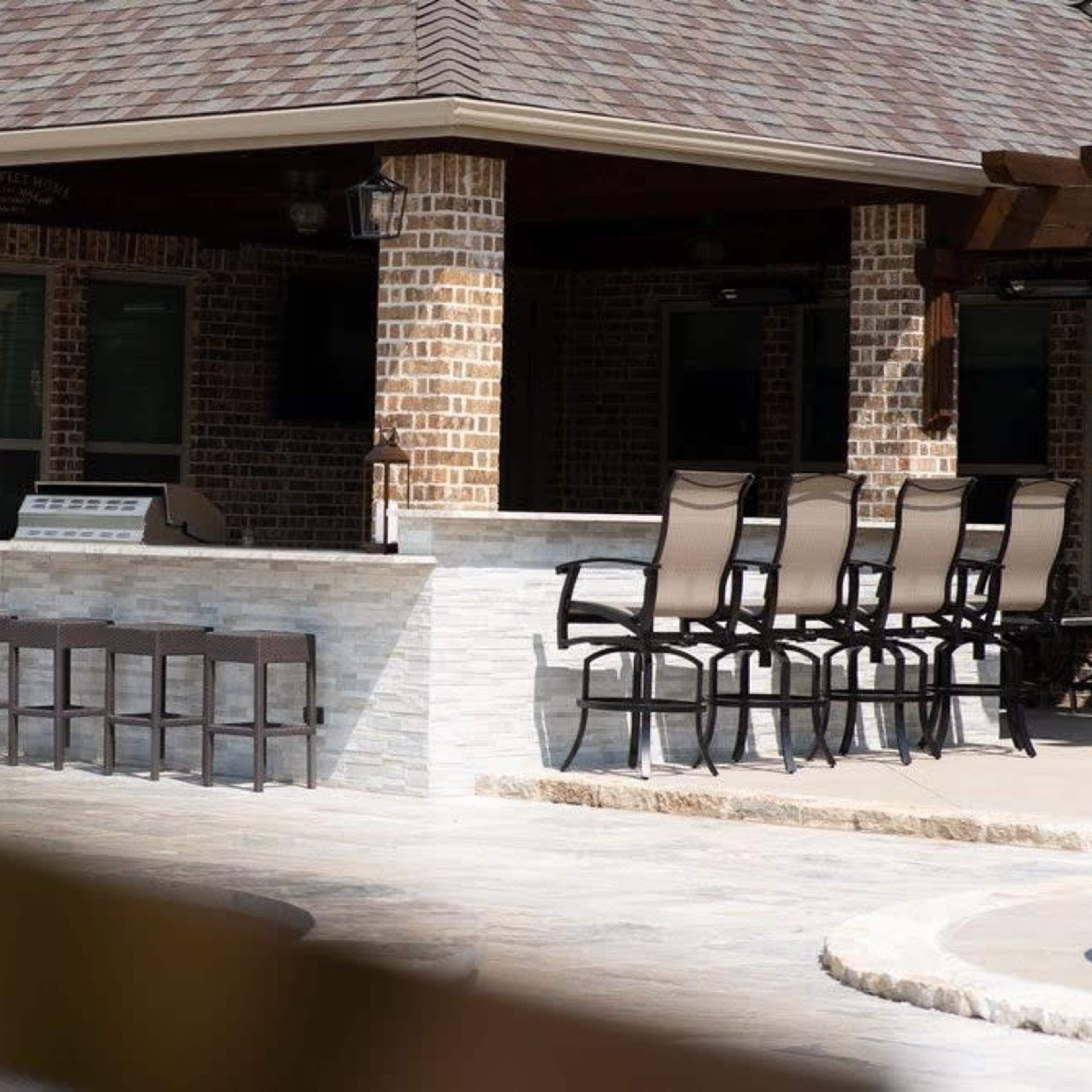 An outdoor bar area with high chairs arranged in front of a stone counter, set within a brick building.