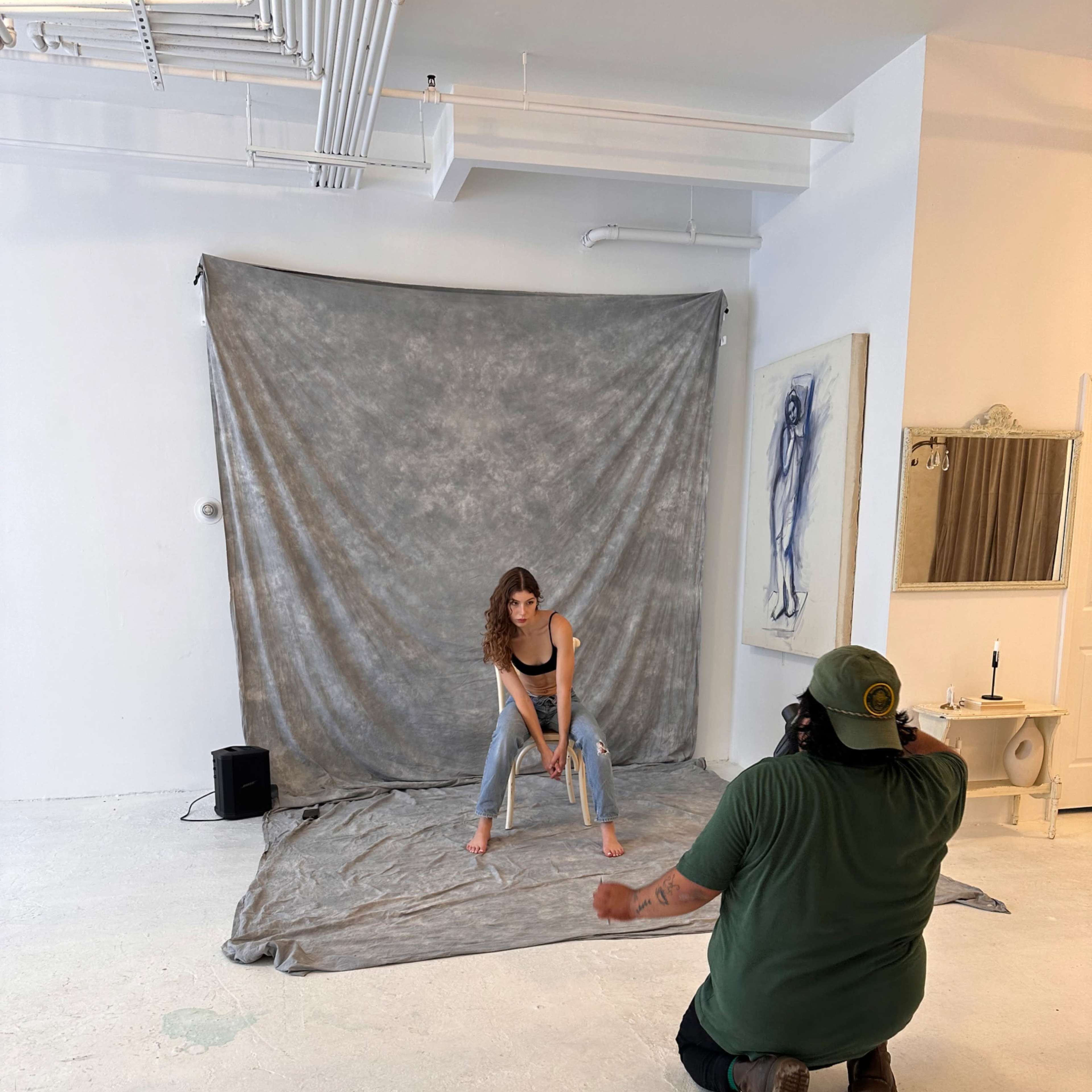 A model poses on a gray backdrop while a photographer captures images in a minimalist studio setting.