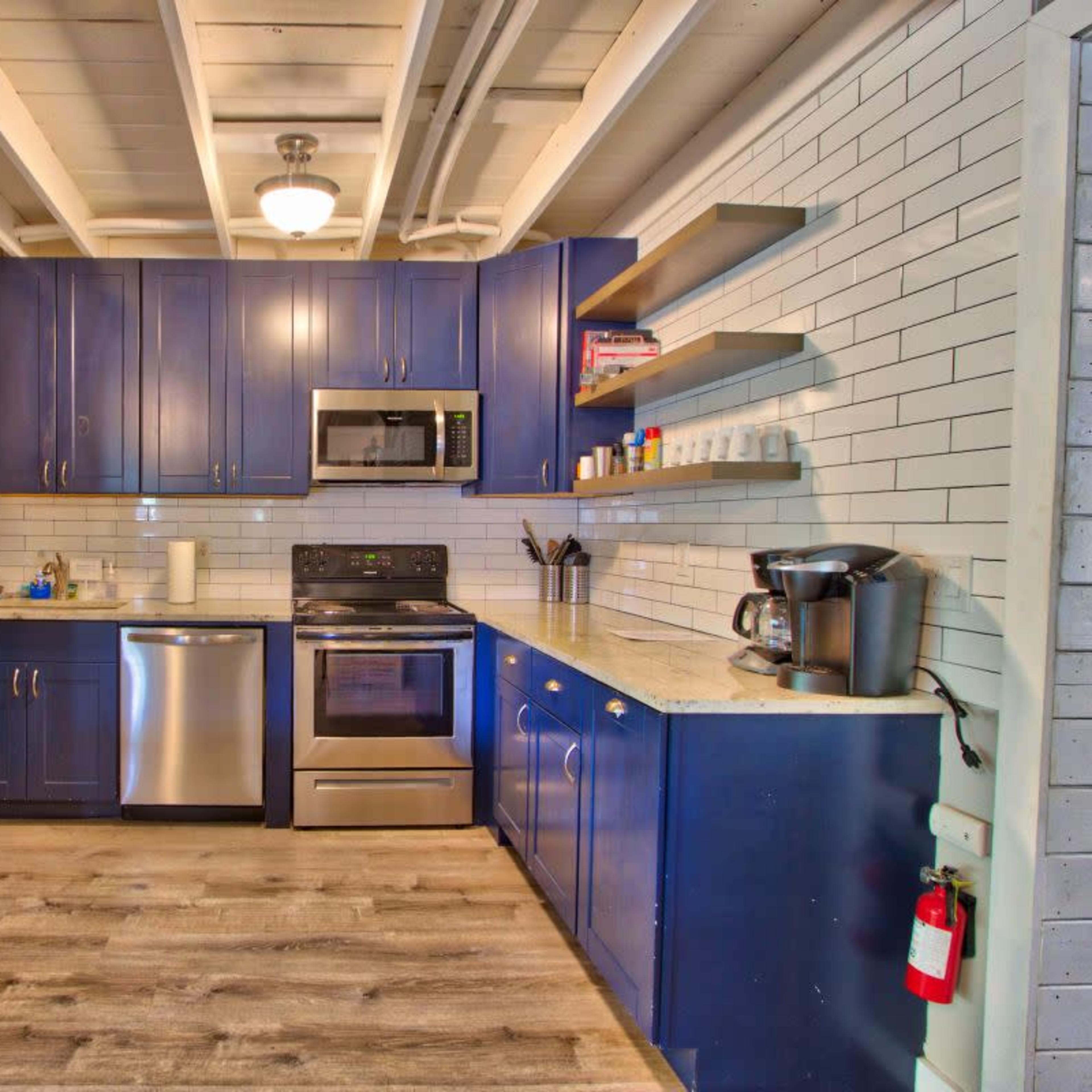 A modern kitchen with navy blue cabinets, stainless steel appliances, and a light-colored countertop.