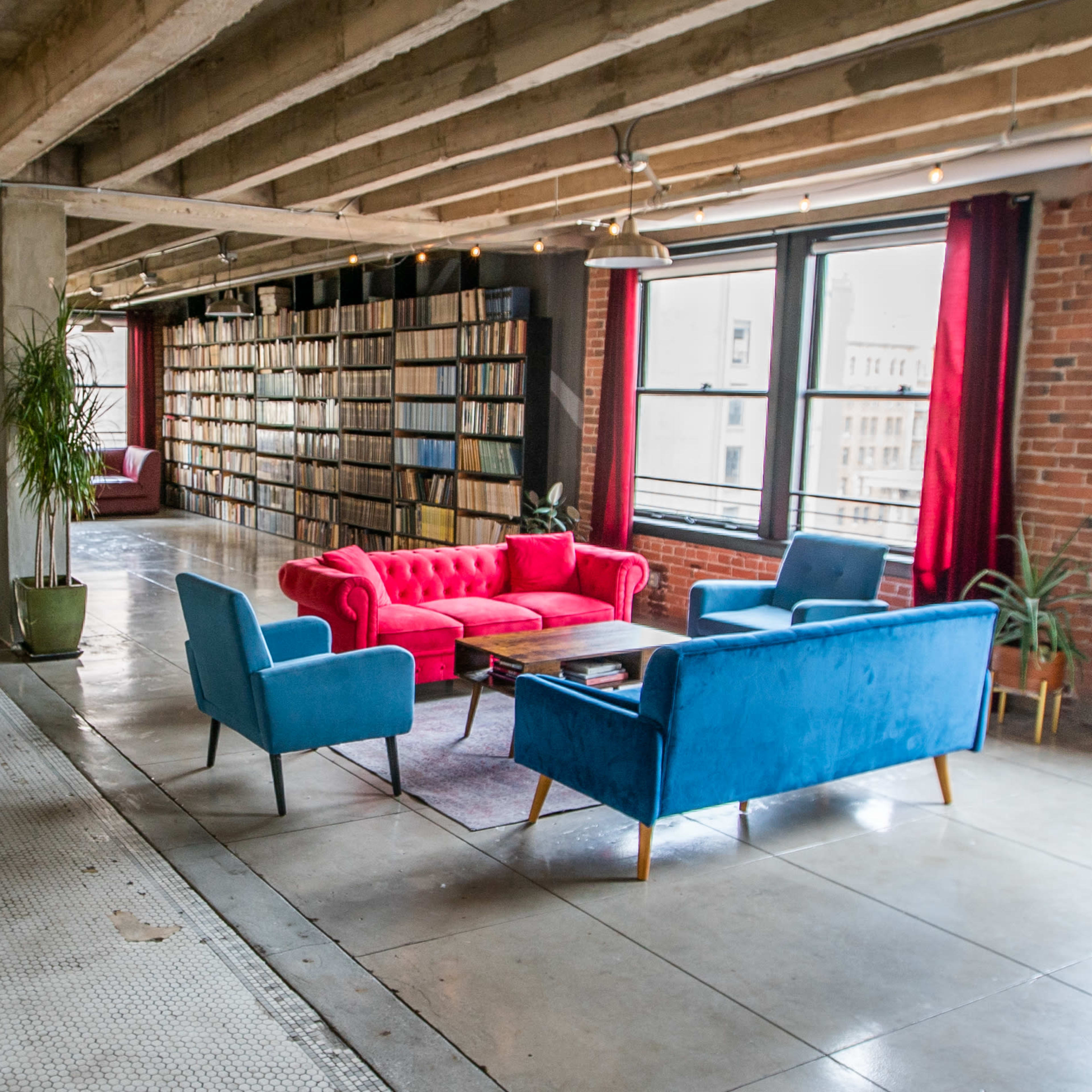 A spacious room with a pink and blue sofa set, surrounded by tall bookshelves filled with books and large windows letting in natural light.