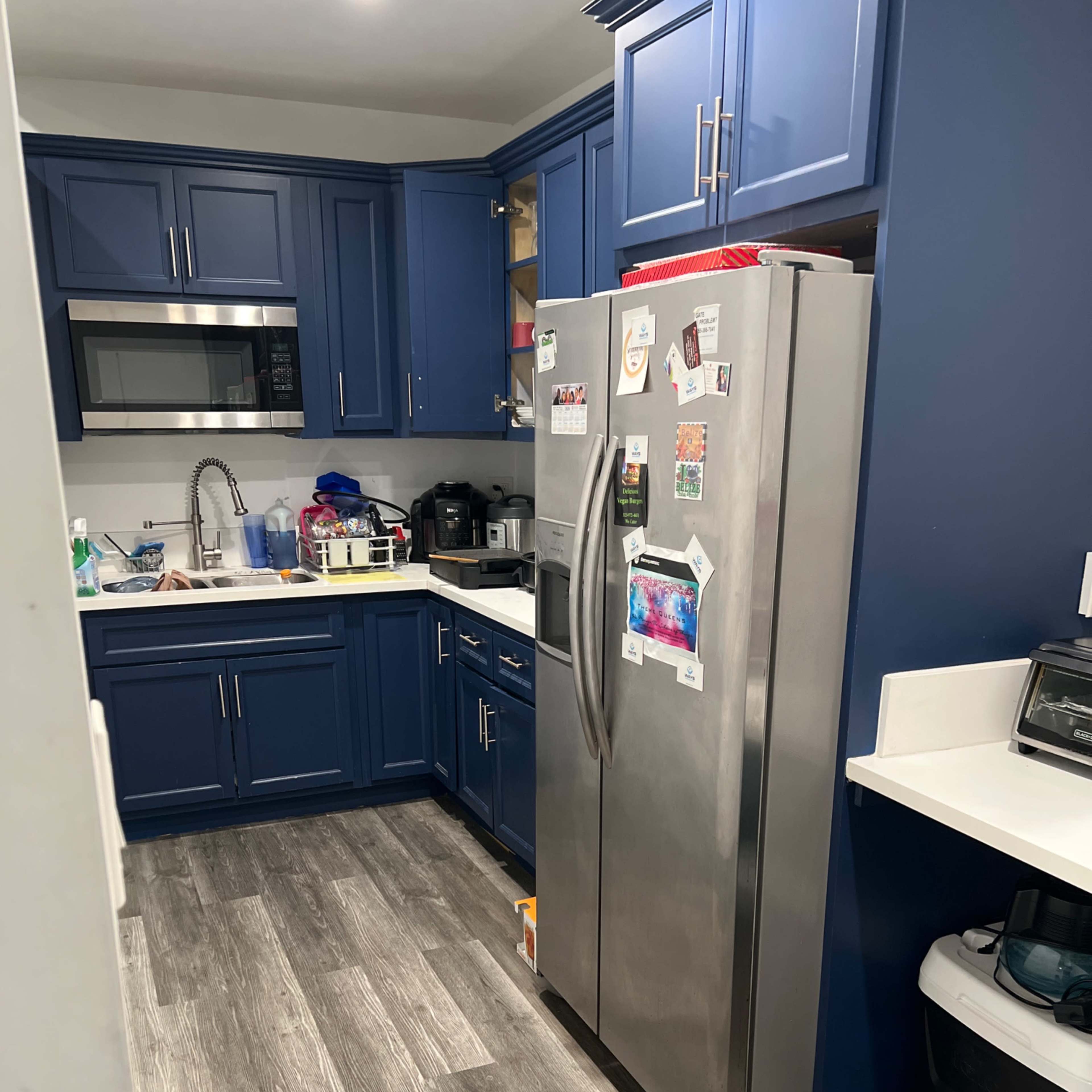 A modern kitchen with blue cabinets, stainless steel appliances, and a mix of countertop items and organizational containers.