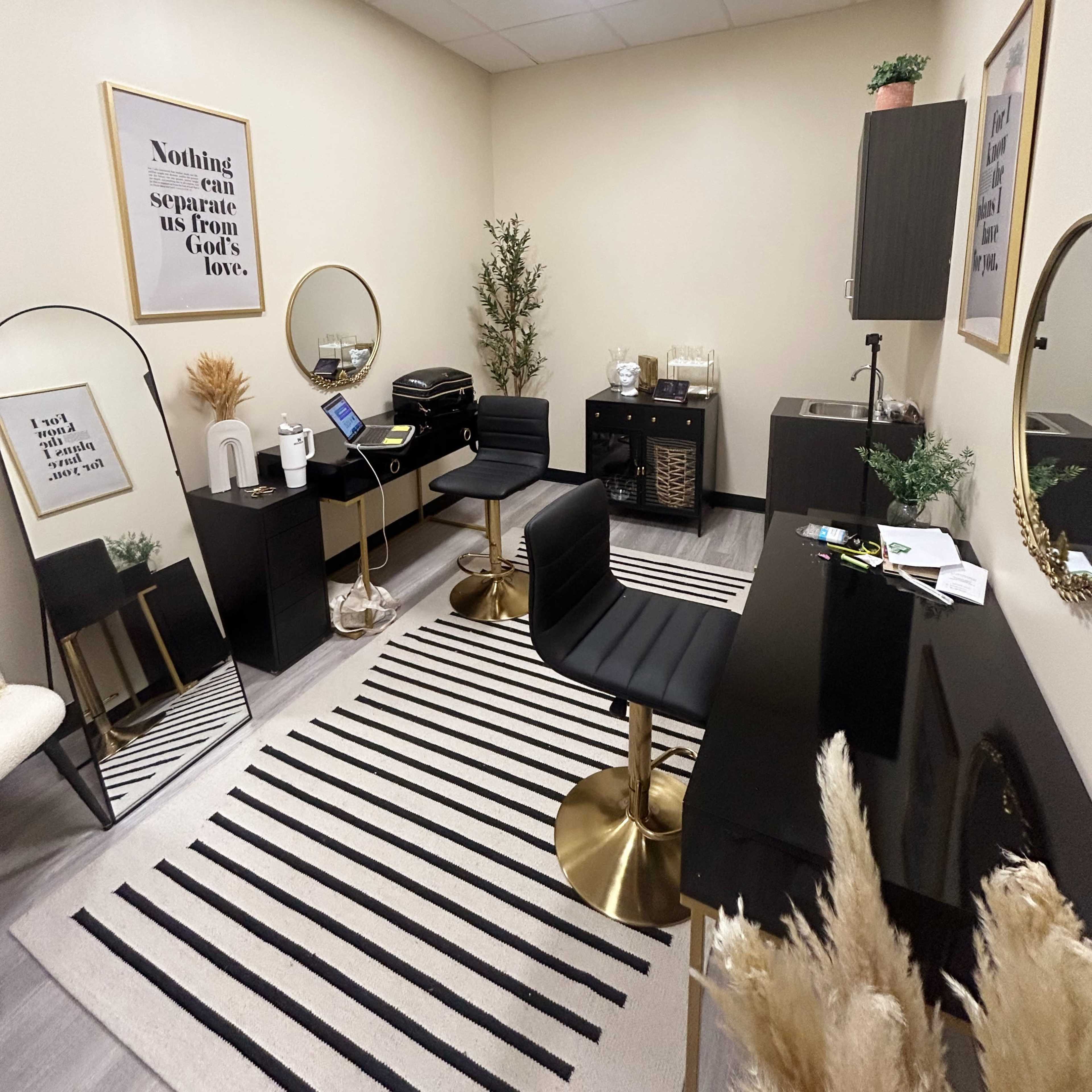 A small, organized room with a desk, two black chairs, a printer, decorative mirrors, and minimalistic decor on the walls.