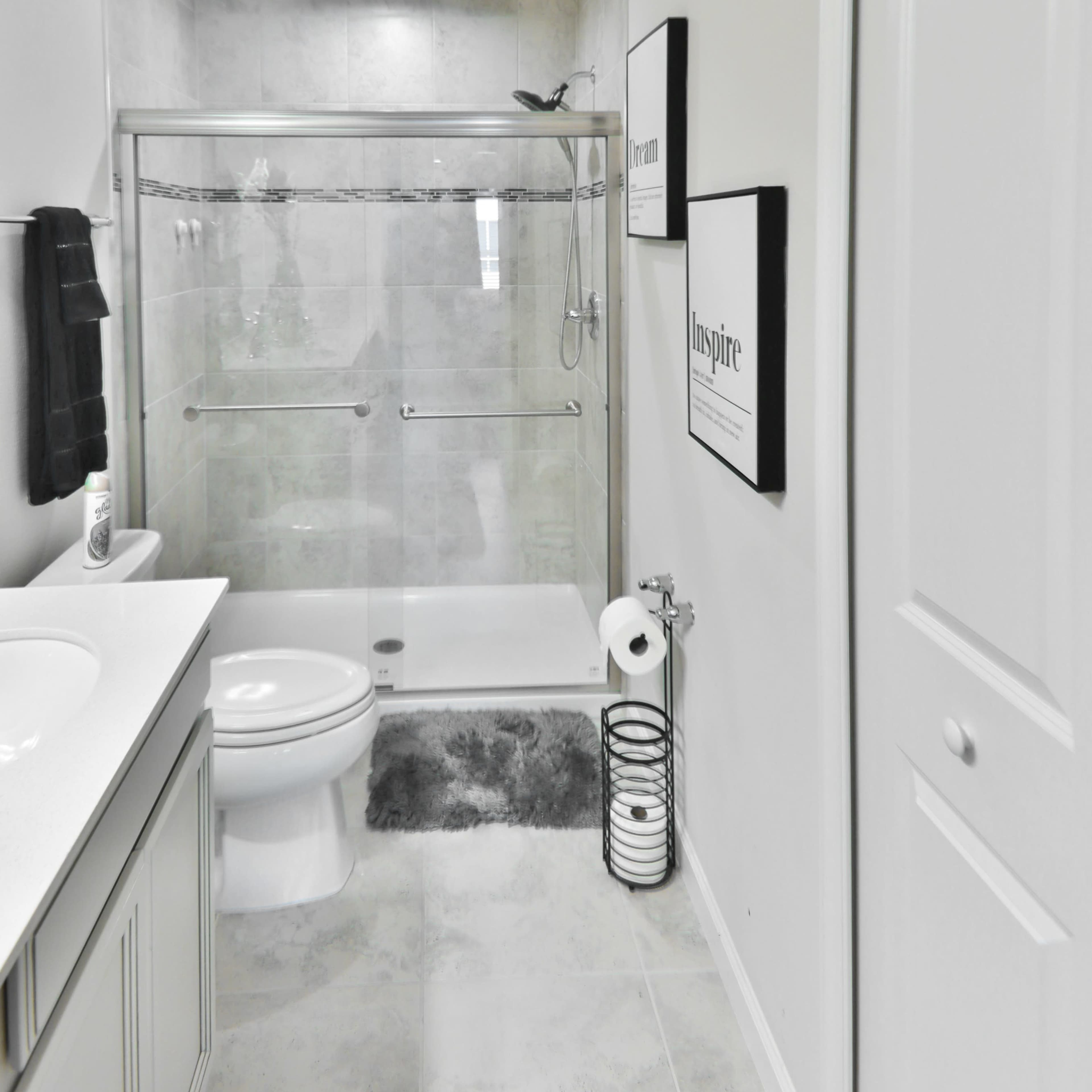 A modern bathroom with a glass shower enclosure, a white sink, and framed motivational artwork on the walls.