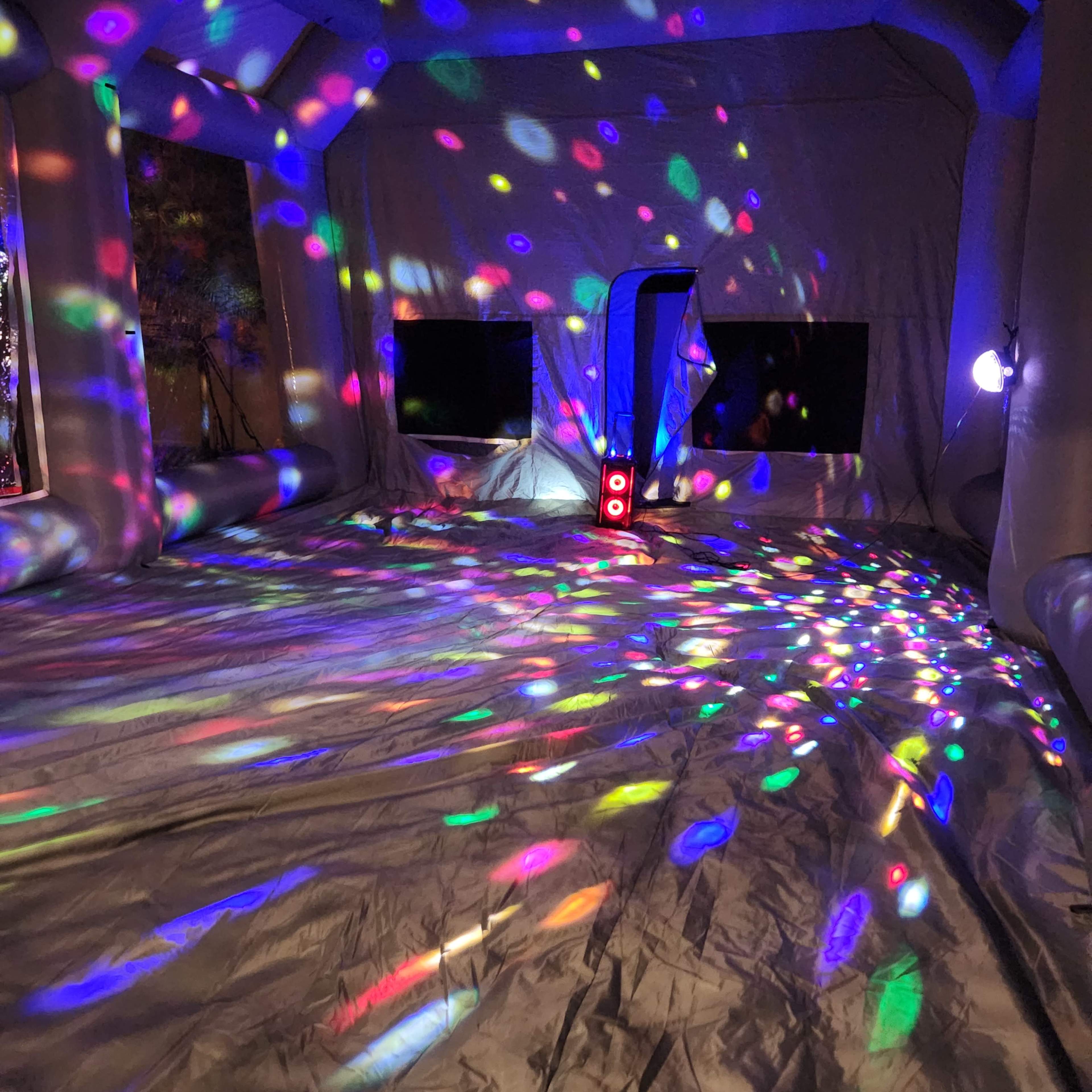 The interior of a large inflatable space features colorful light patterns on the walls and floor, created by a disco ball or light projector.