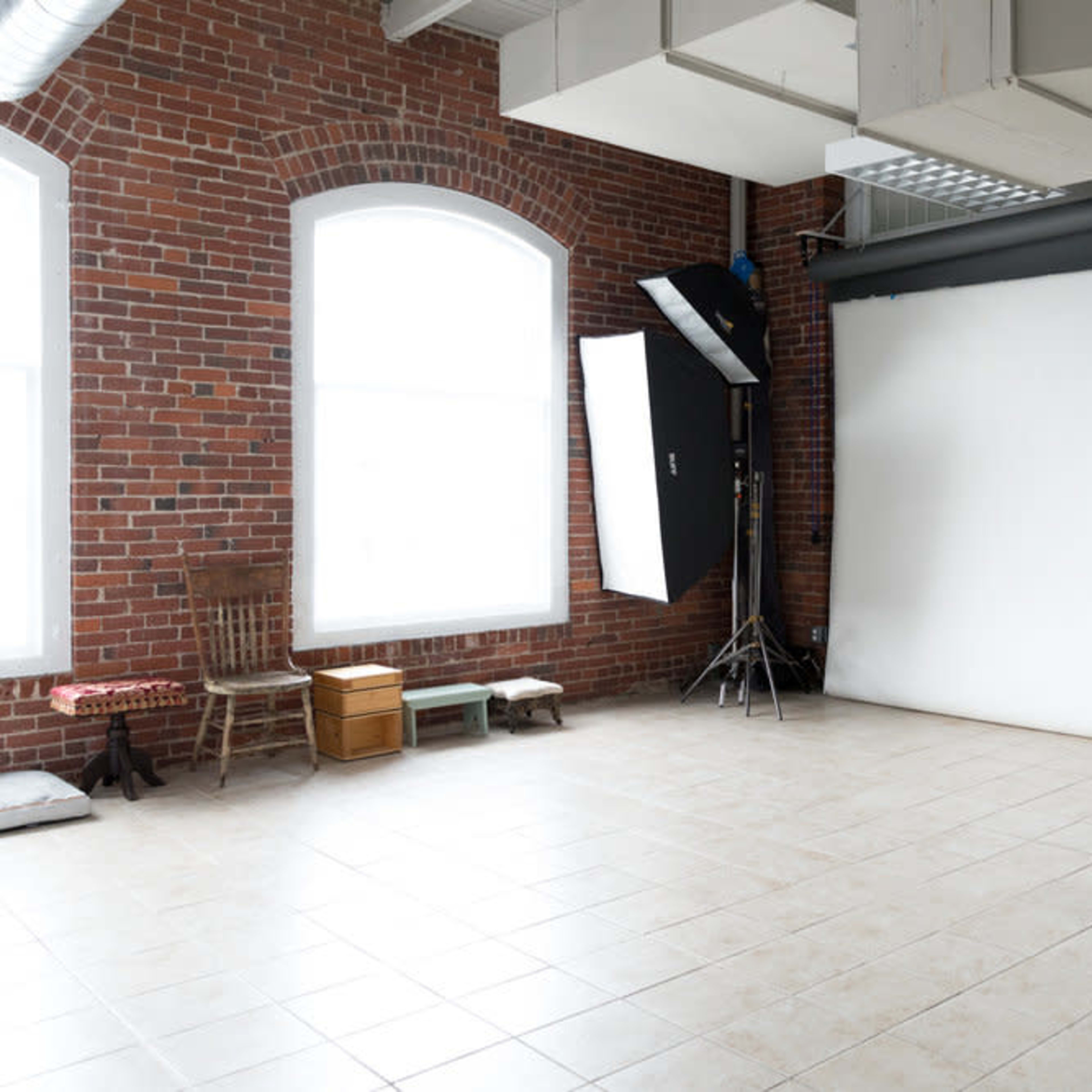 A spacious photography studio features exposed brick walls, a white backdrop, and multiple lighting setups.