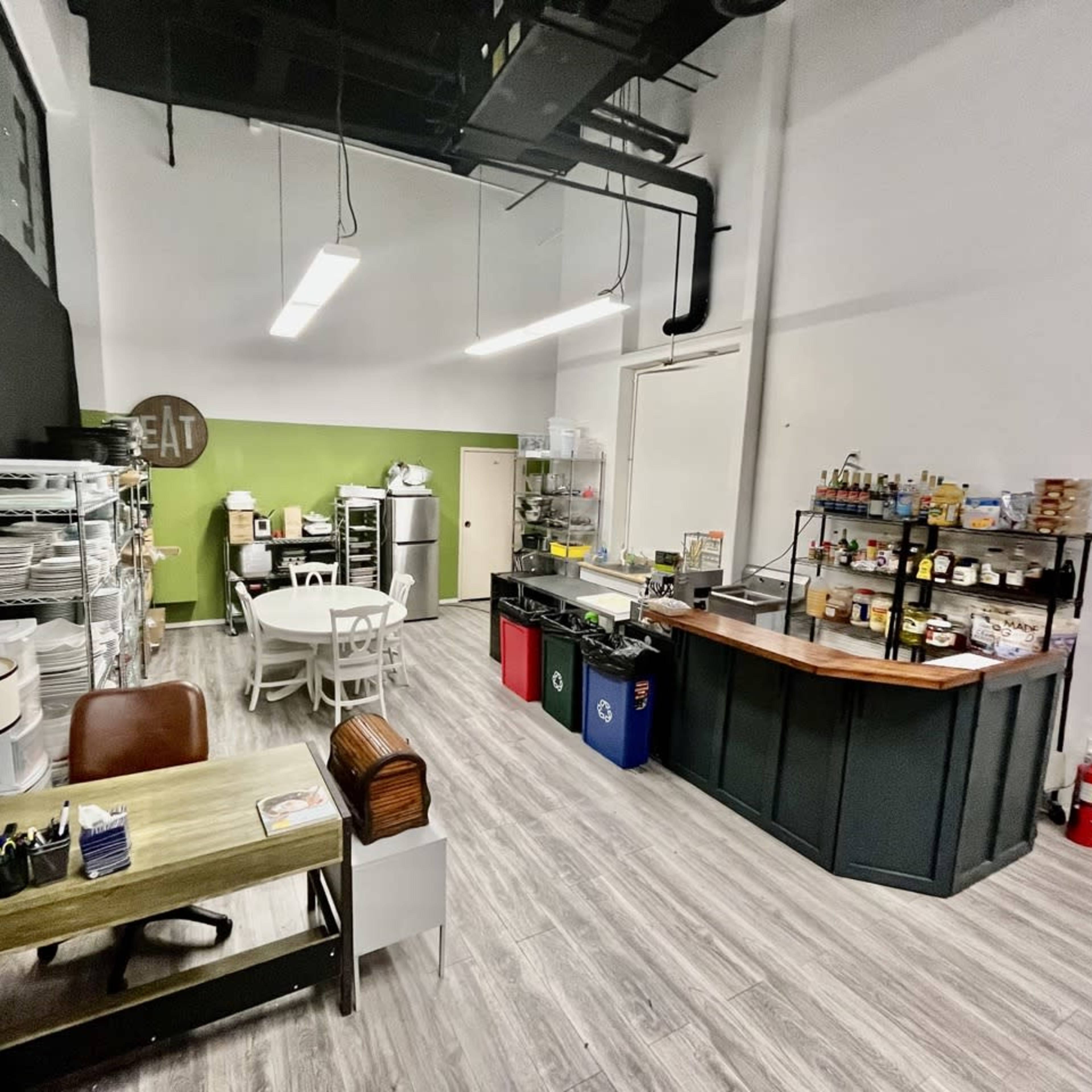 A spacious commercial kitchen area featuring a seating table, workstations, storage shelves, and a service counter.
