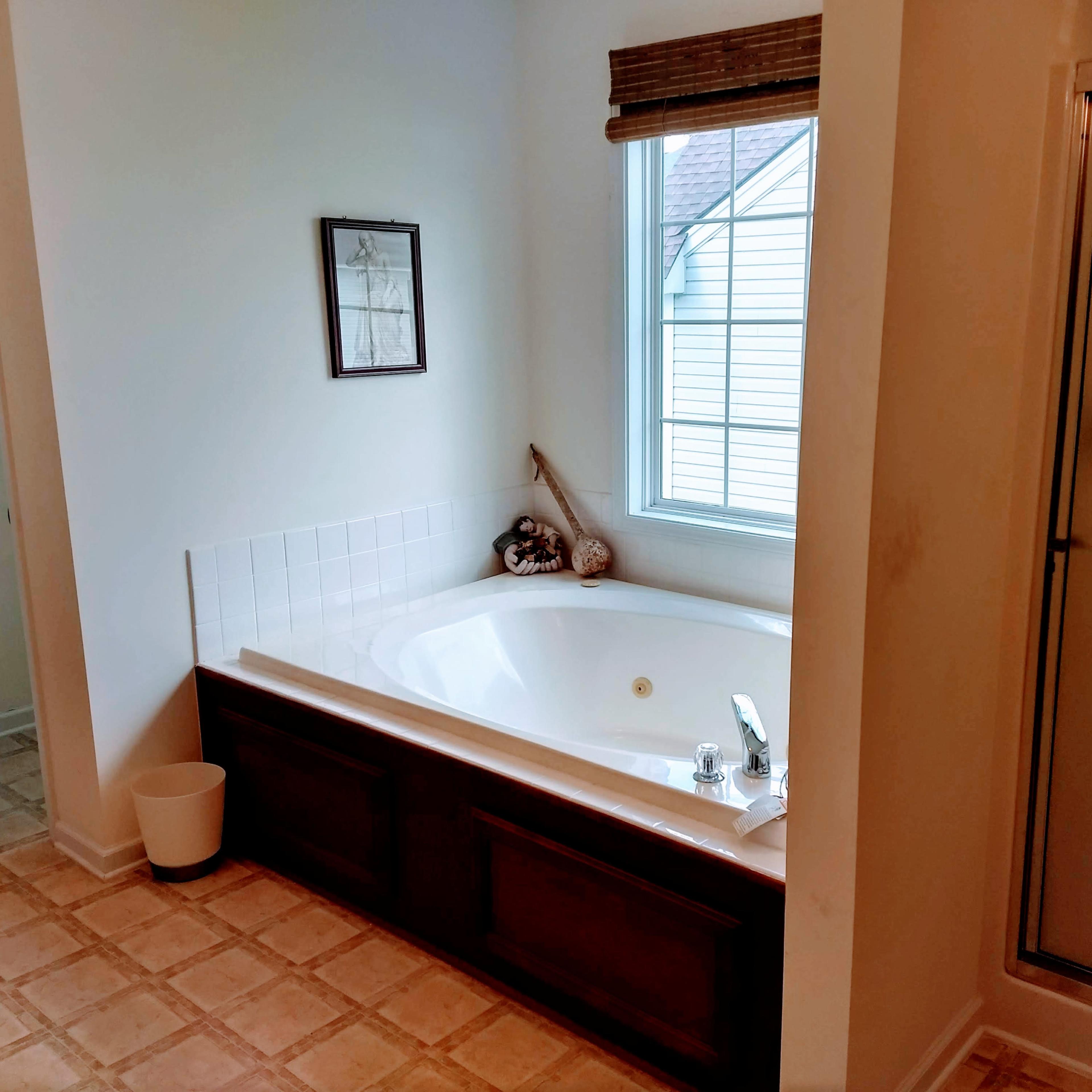 A bathroom with a large corner bathtub, a shower stall, and a window allowing natural light to enter.