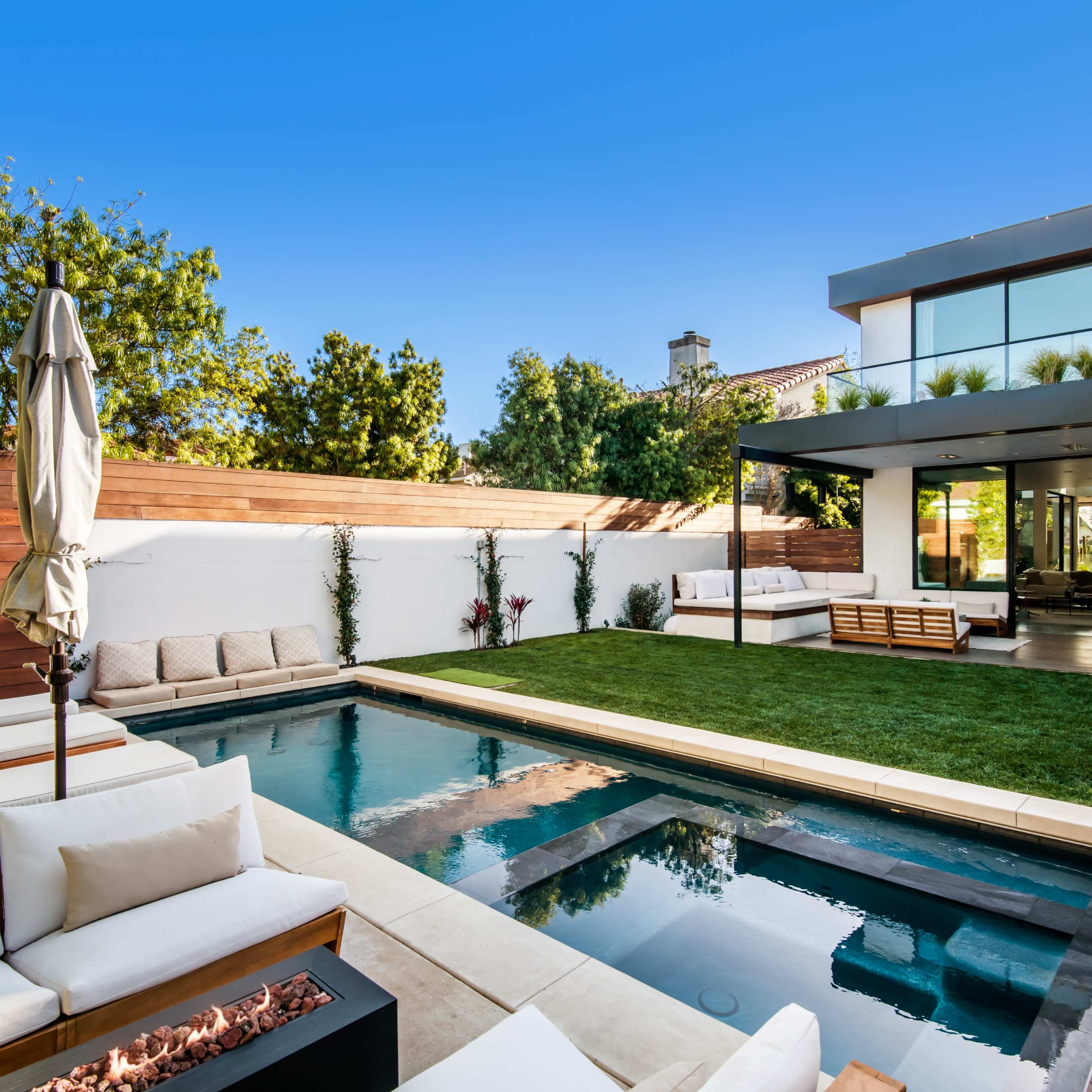 A modern backyard features a pool surrounded by lounge chairs, a grassy area, and a sleek outdoor living space.