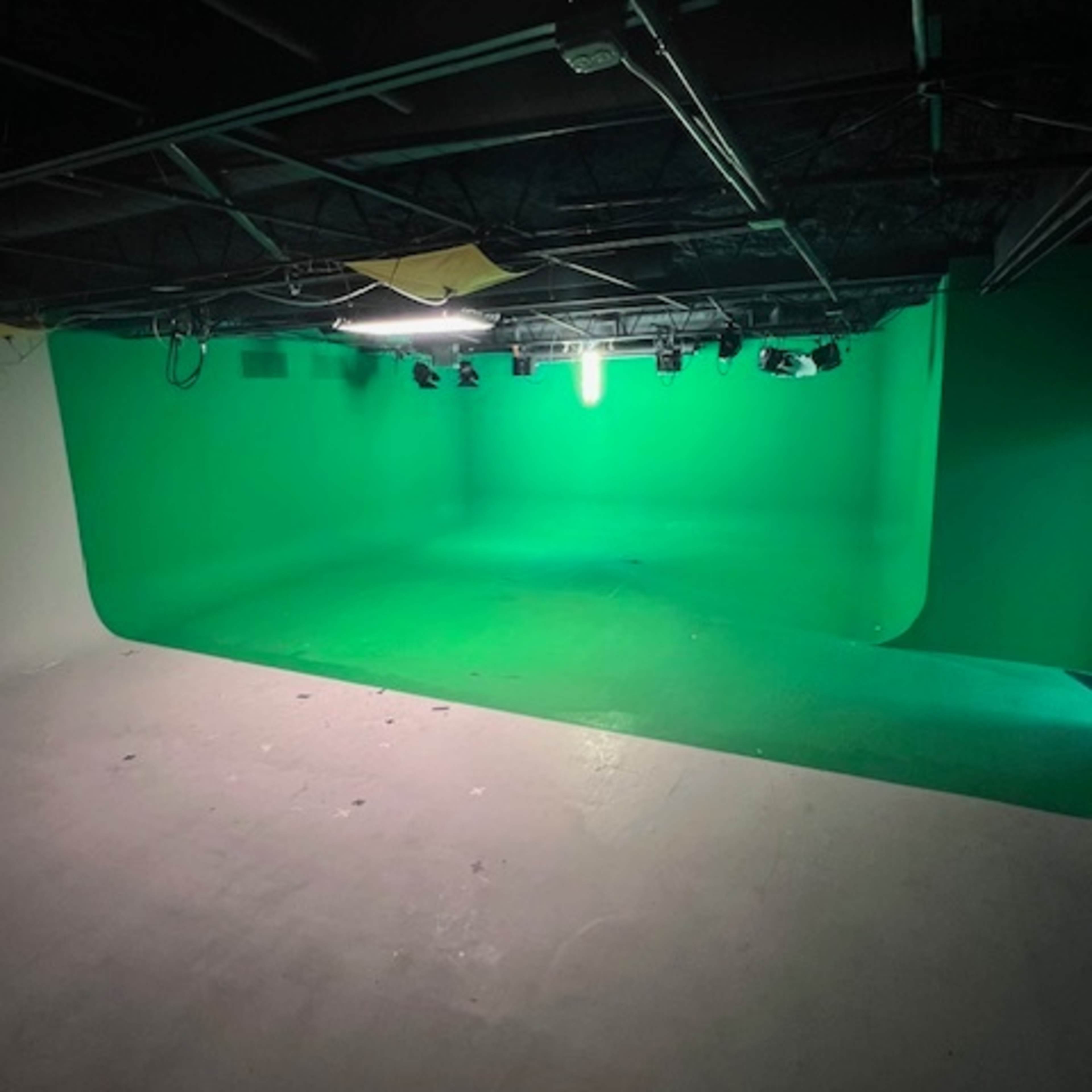 An empty studio with a green screen backdrop and overhead lighting.