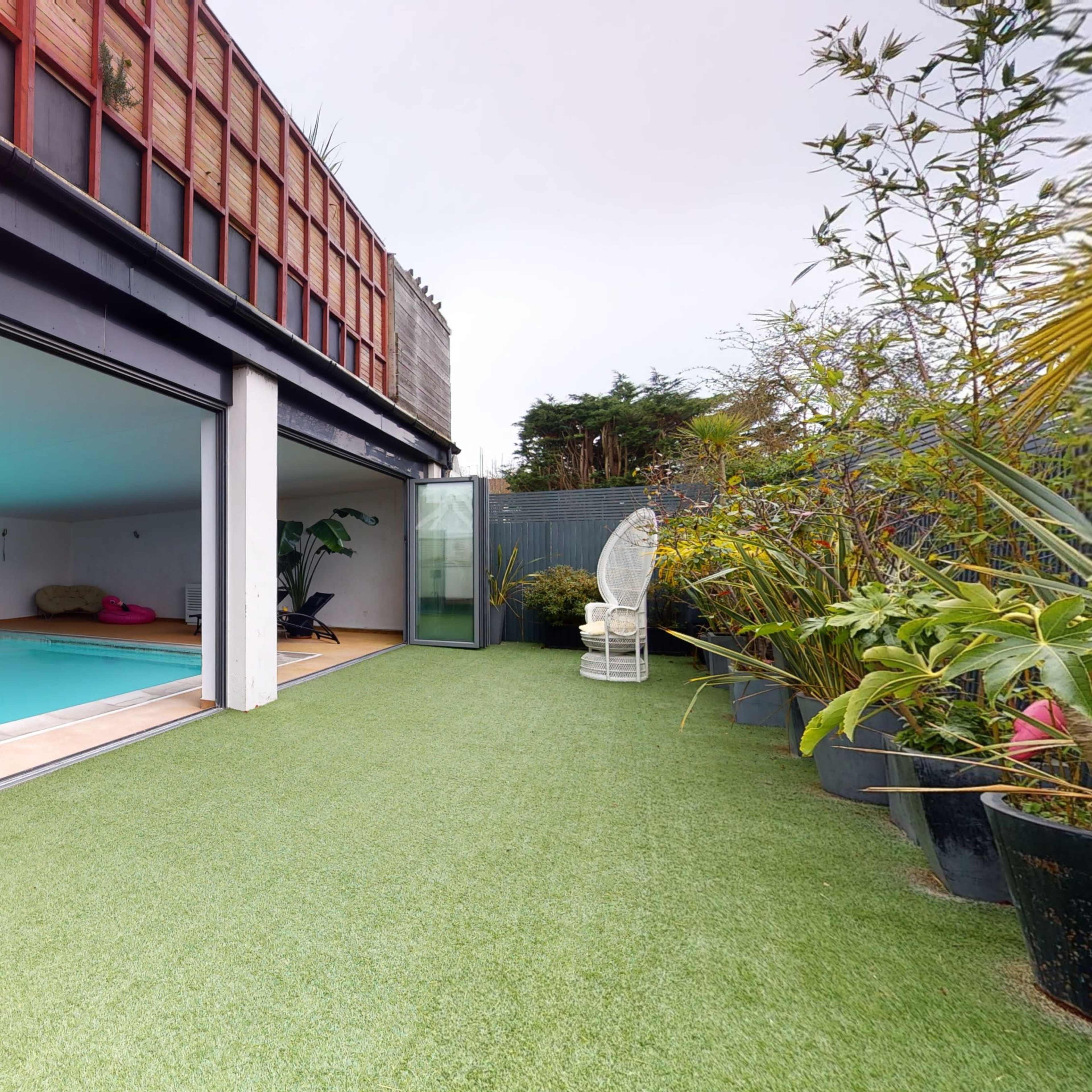 A modern indoor pool area with a grassy outdoor space and a statue surrounded by plants.