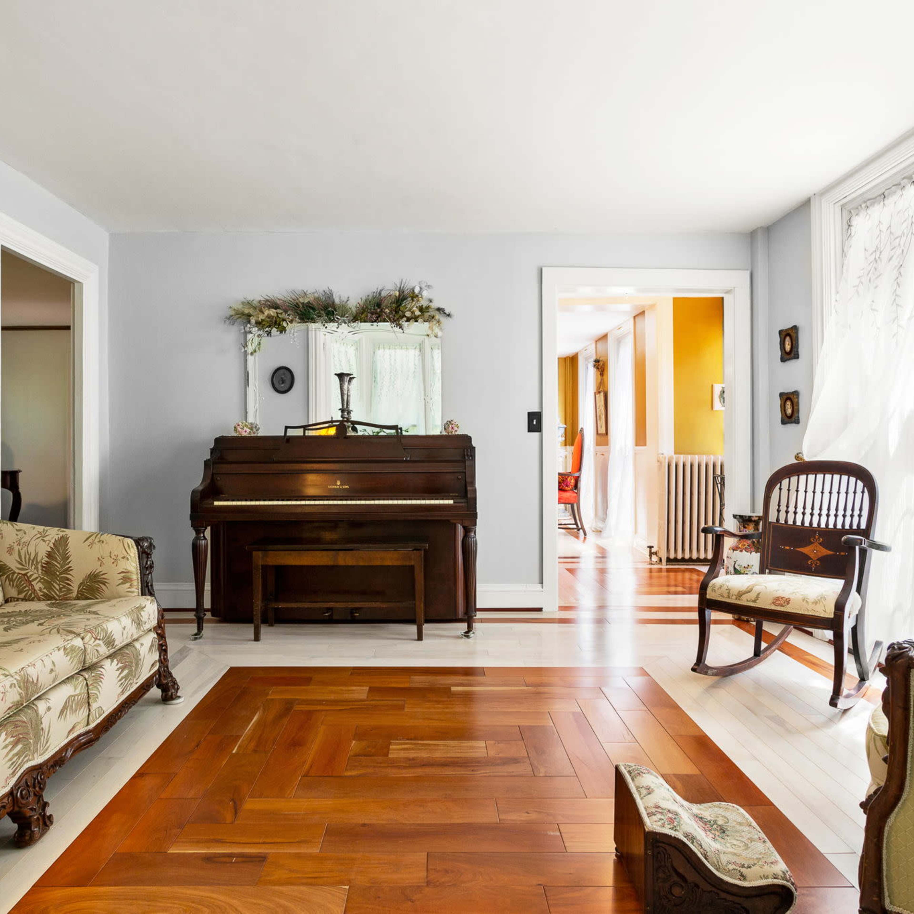 A living room featuring a piano, a patterned sofa, and wooden flooring.