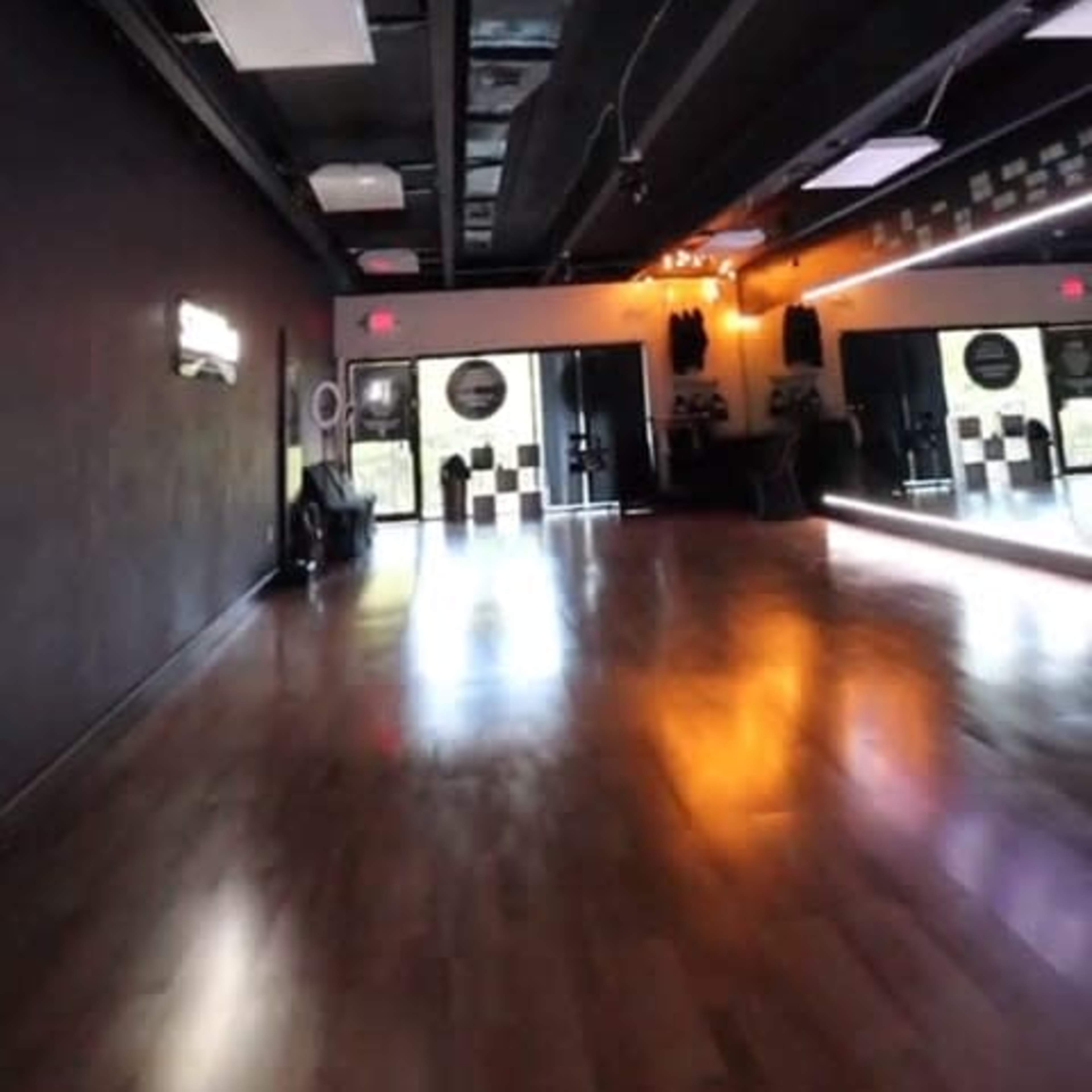 An empty dance studio with polished wooden floors and mirrored walls, illuminated by soft ceiling lights.