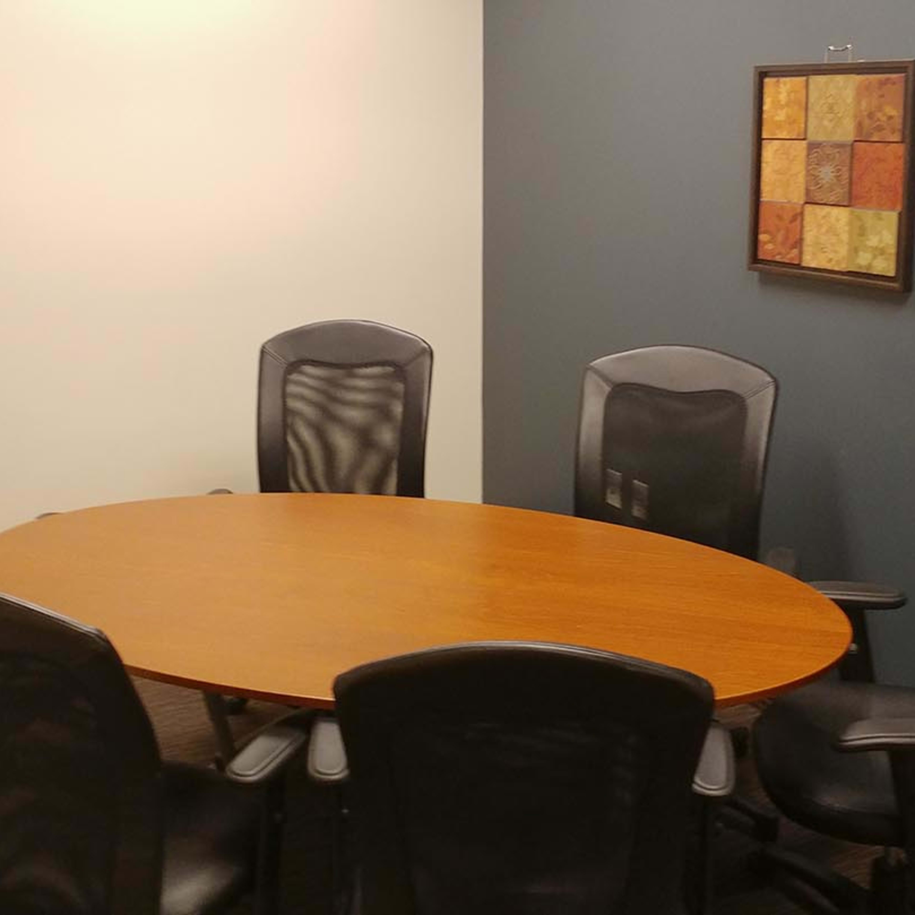 A round wooden conference table is surrounded by six black office chairs in a small meeting room.