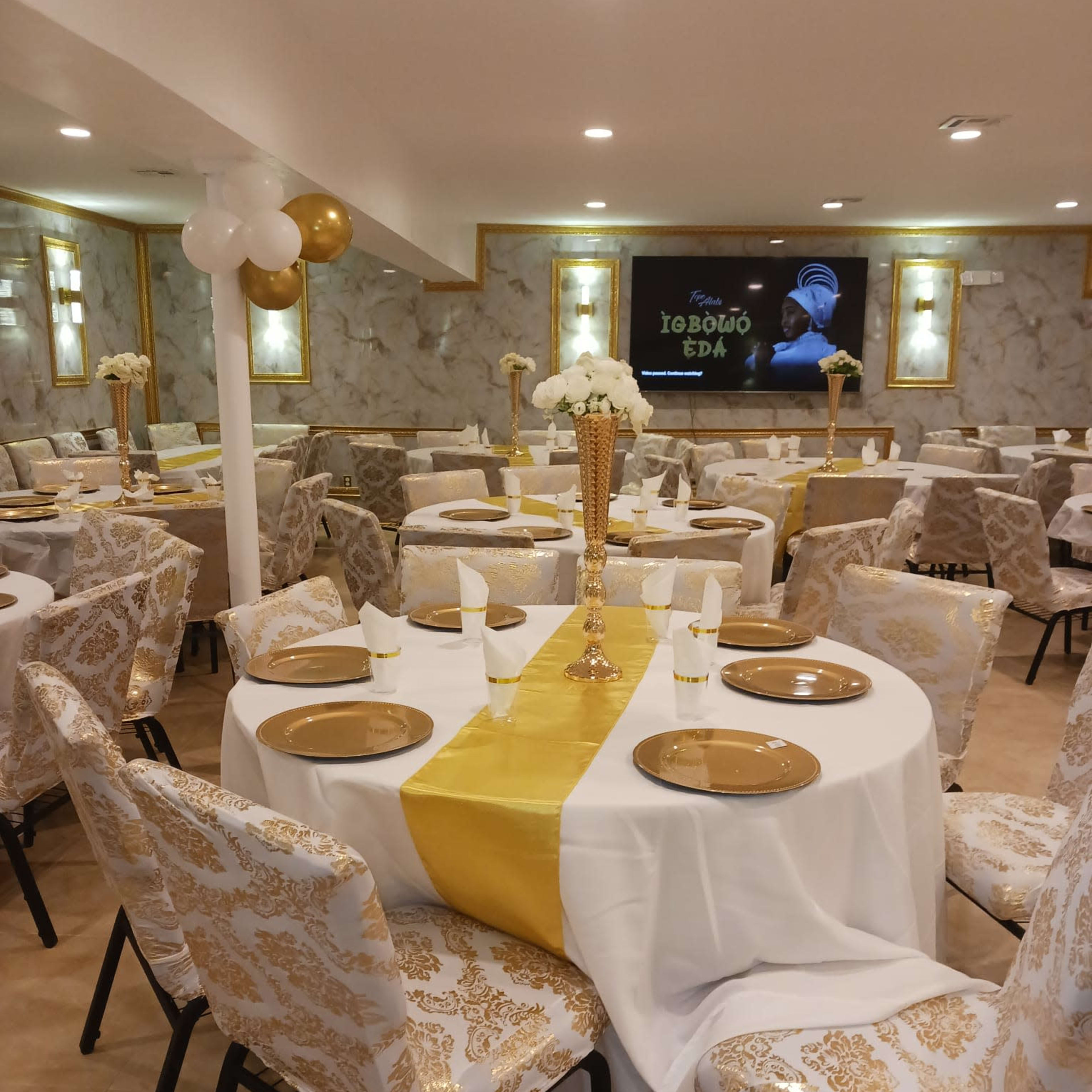A well-decorated banquet hall with tables set for an event, featuring white and gold table linens and chairs.
