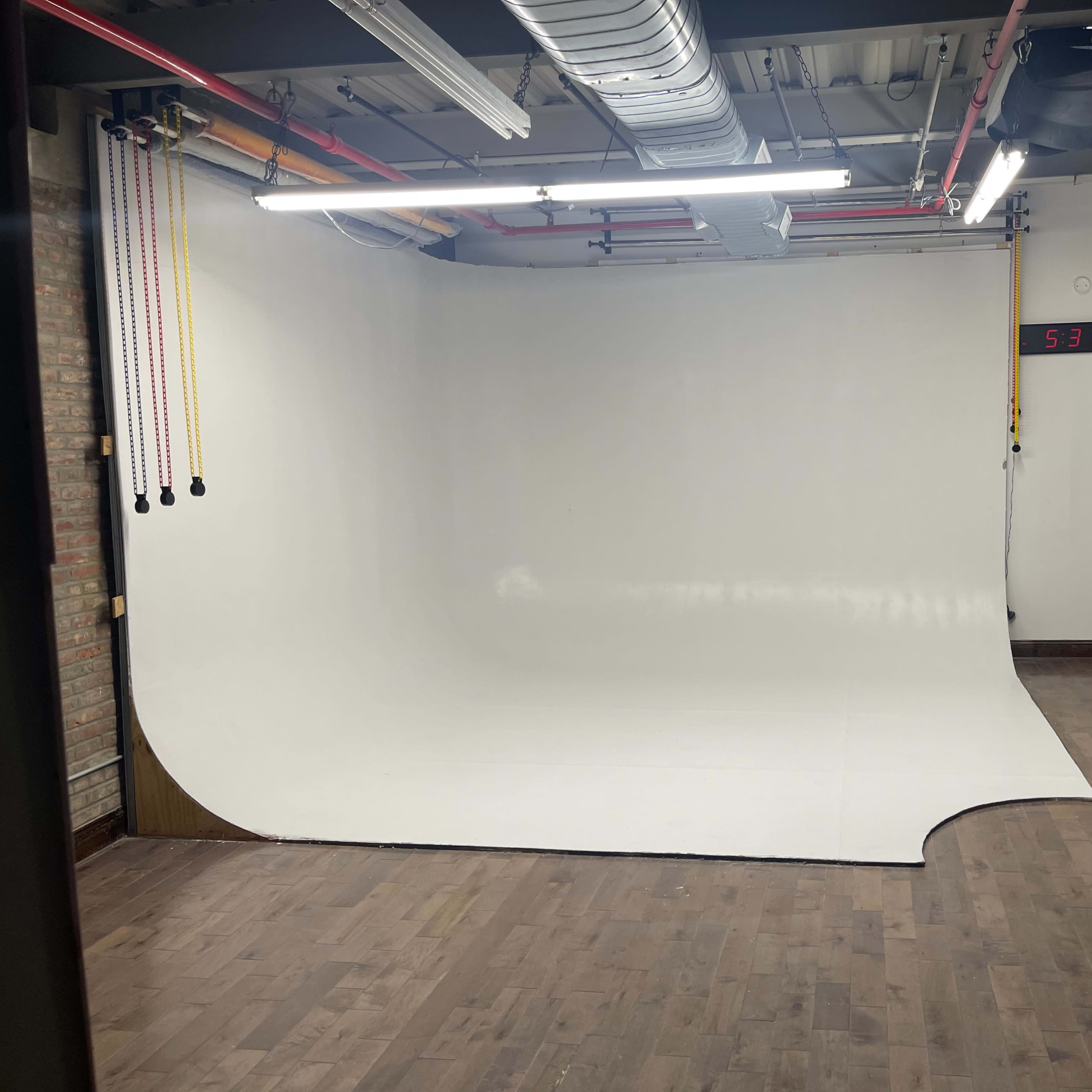 A minimalistic photo studio with a large white seamless backdrop and wooden flooring.