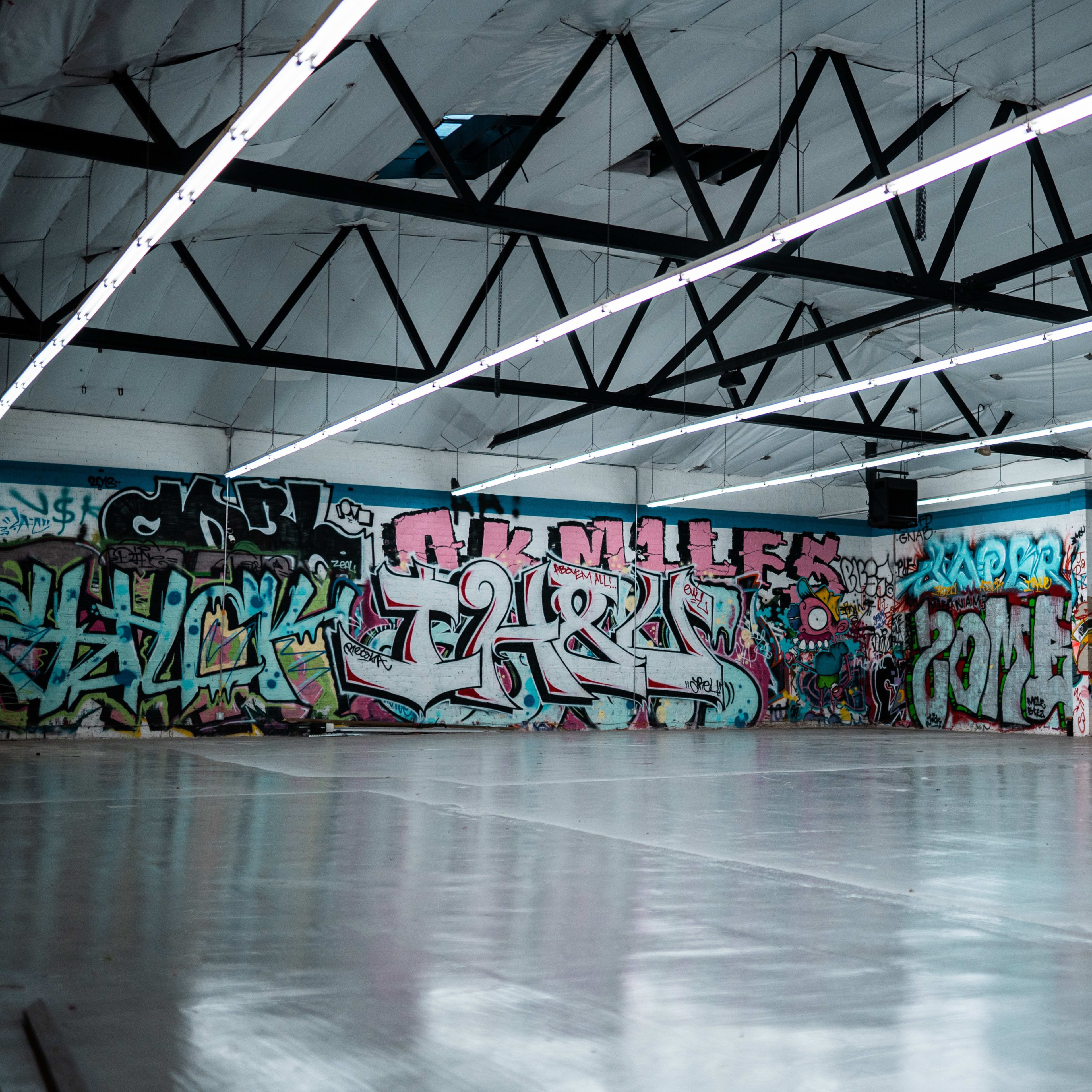 An industrial space with bare concrete flooring and walls covered in various styles of colorful graffiti.