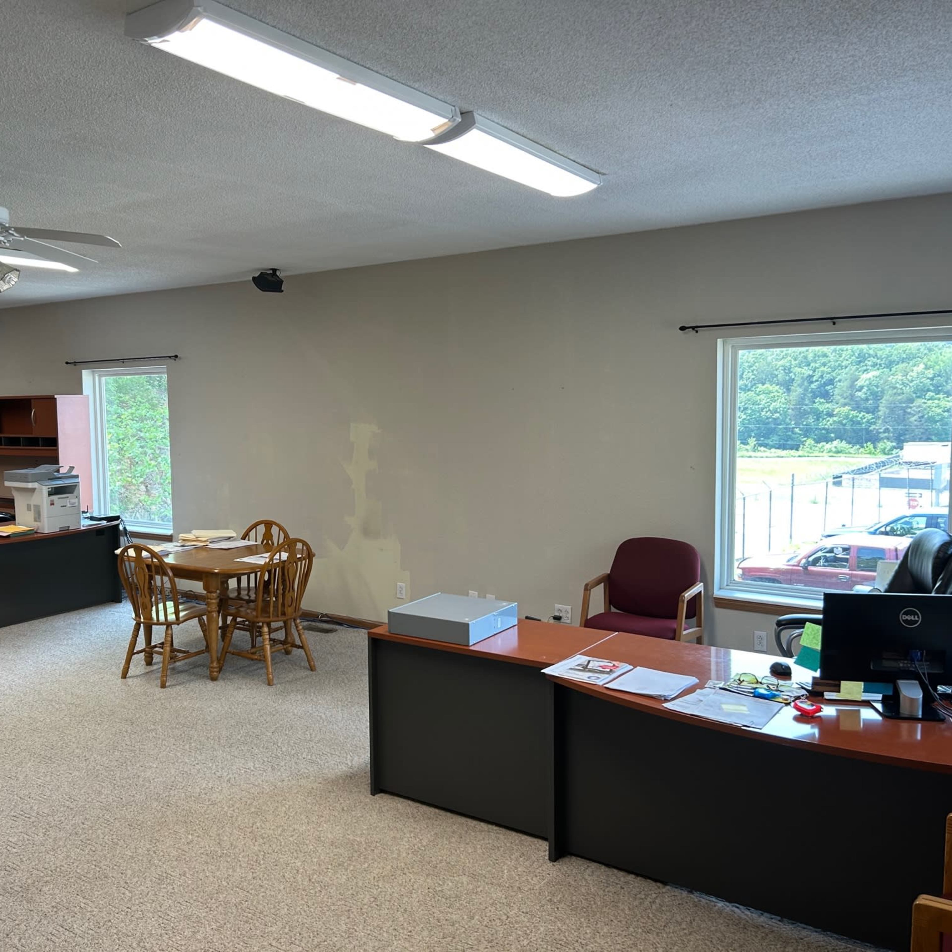 An office space with kitchen facilities, a dining area with a table and chairs, and two desks with office equipment.