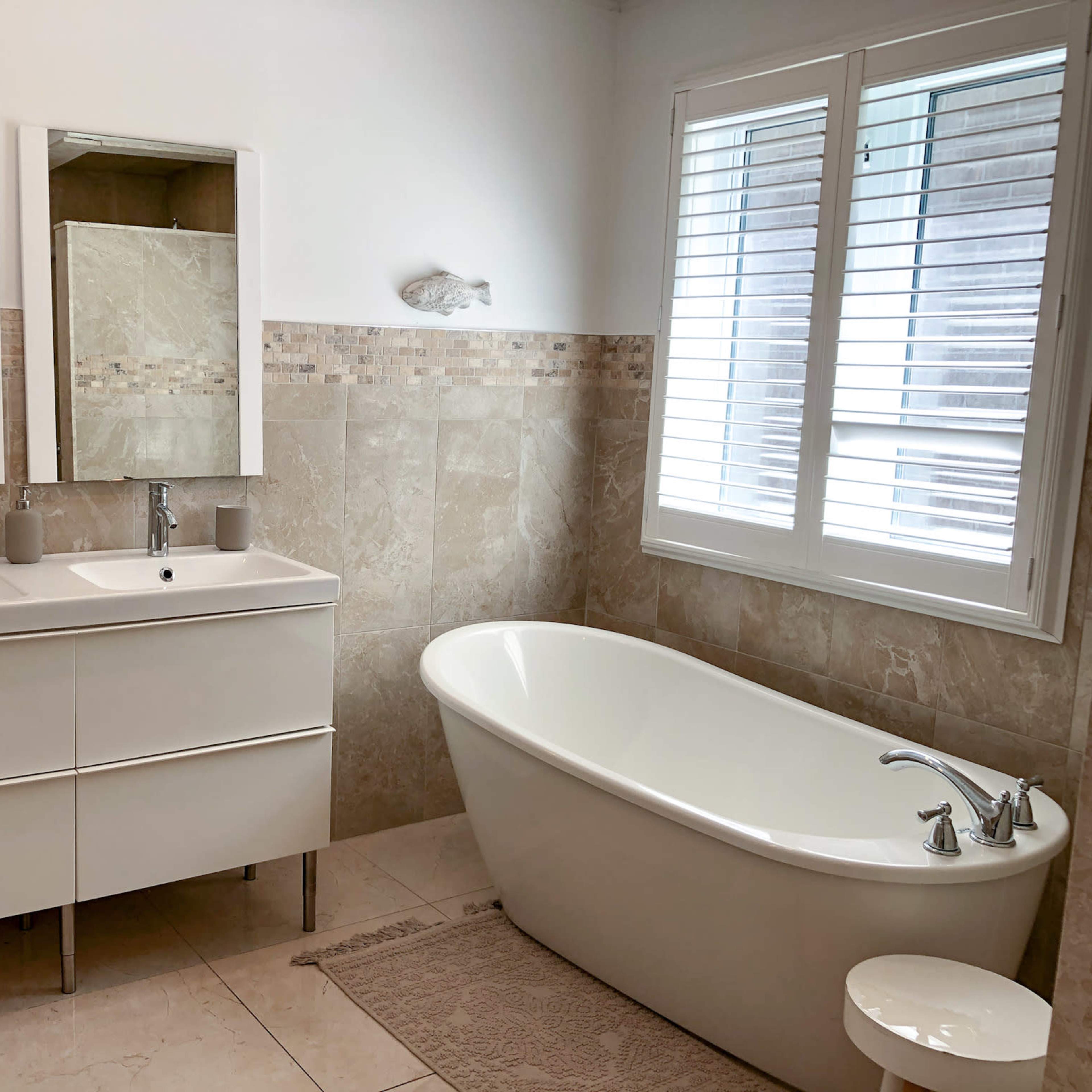 The bathroom features a double sink vanity with mirrors, a freestanding bathtub, and tiled walls with a neutral color scheme.