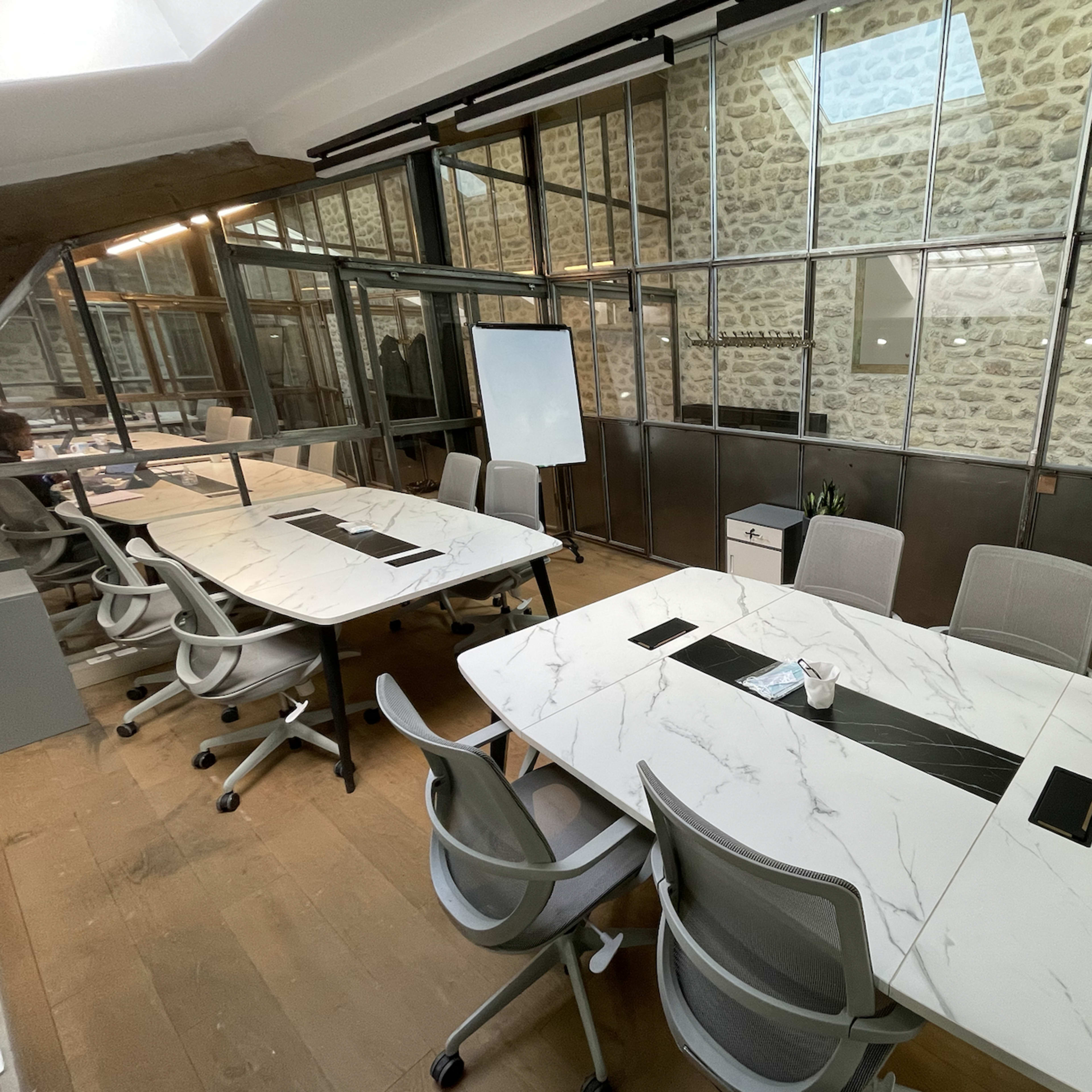A modern office space featuring glass-walled meeting rooms with marble-topped tables and ergonomic chairs.