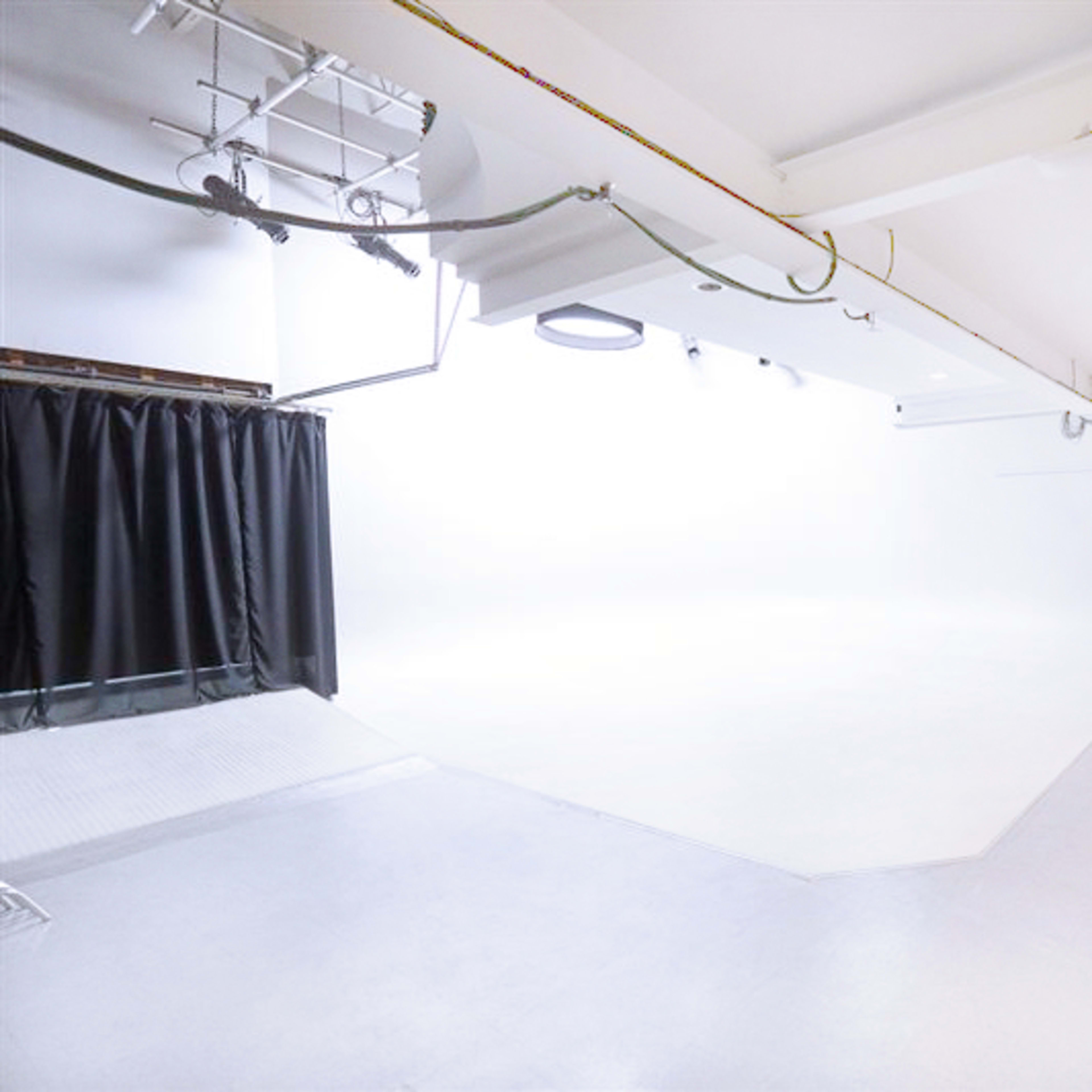 A spacious, well-lit studio with a white backdrop, a table, and a chair on a light-colored floor.