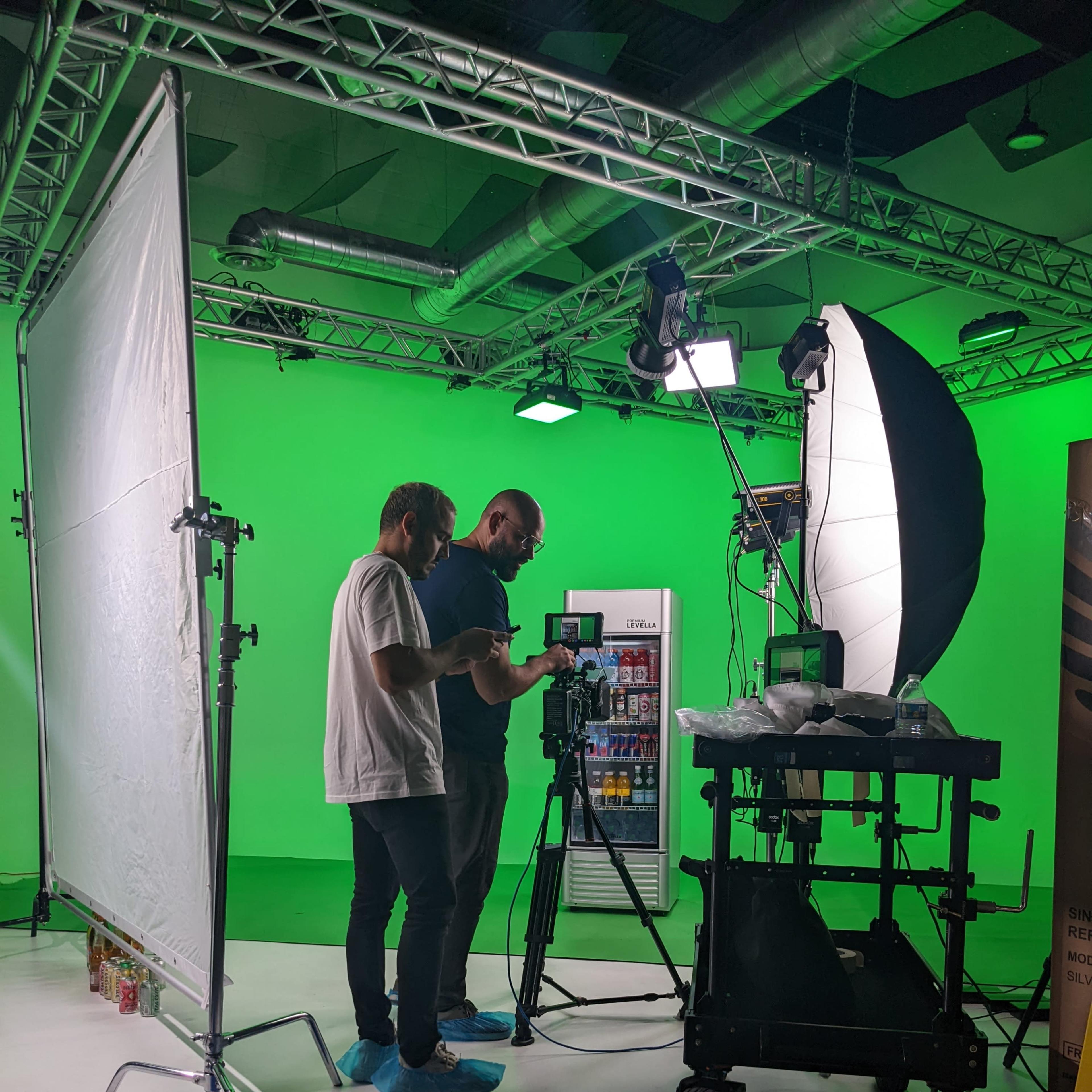 Two individuals are setting up a camera and equipment in a studio with a green screen backdrop.