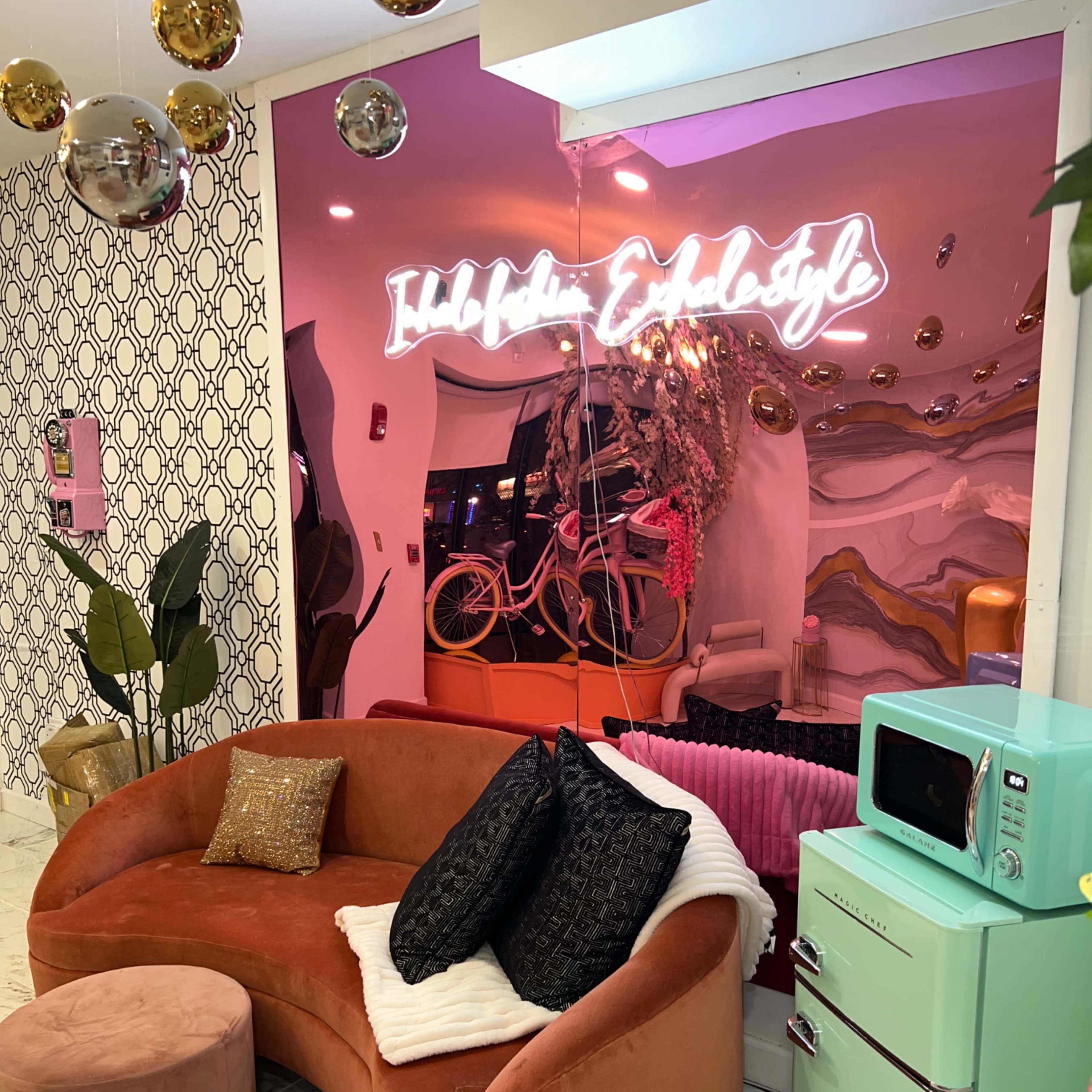 A cozy seating area featuring a curved peach-colored couch, green retro-style refrigerator, and a neon sign displaying "Hello Beautiful" against a colorful backdrop.