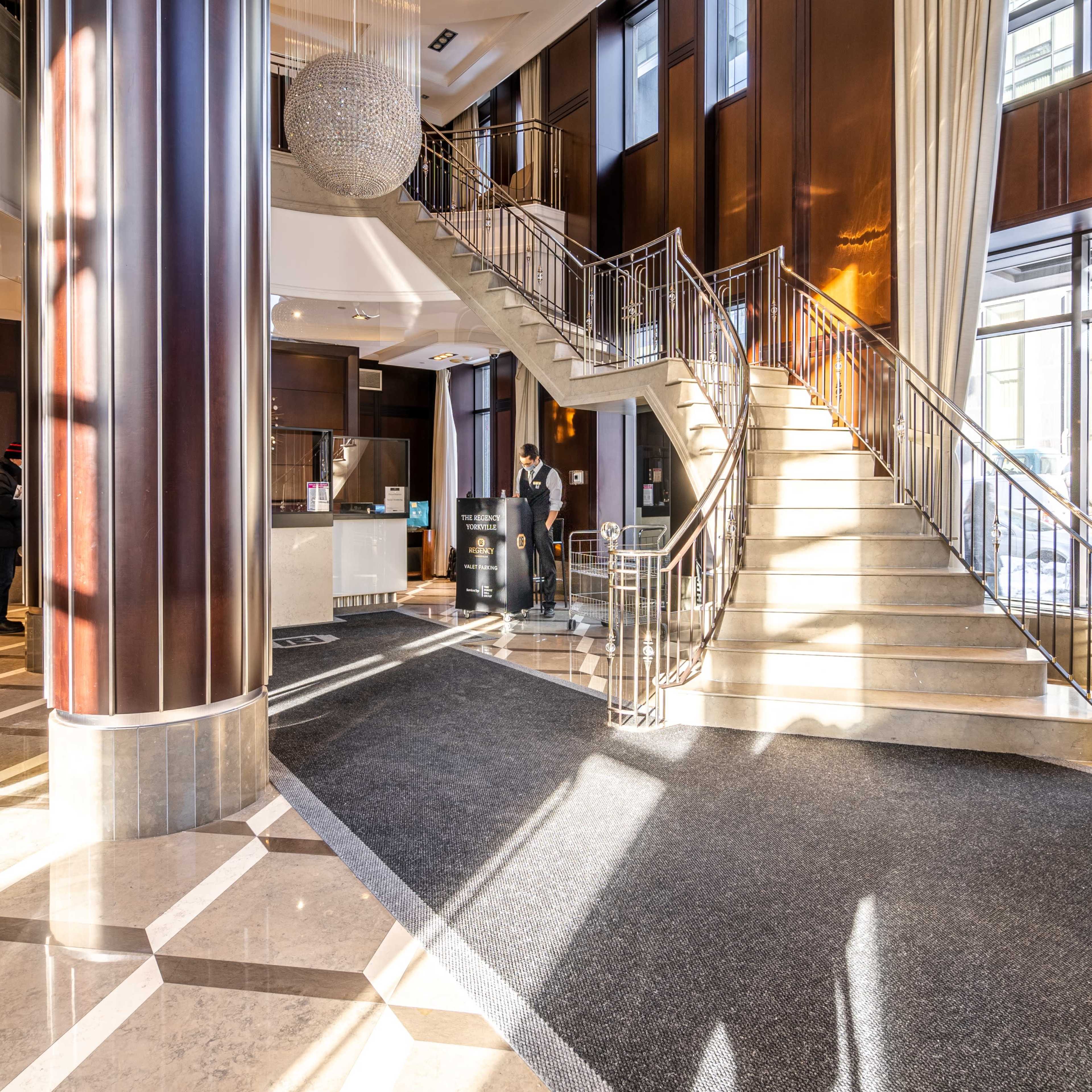 A spacious hotel lobby with a grand staircase, polished marble floors, and modern furnishings.