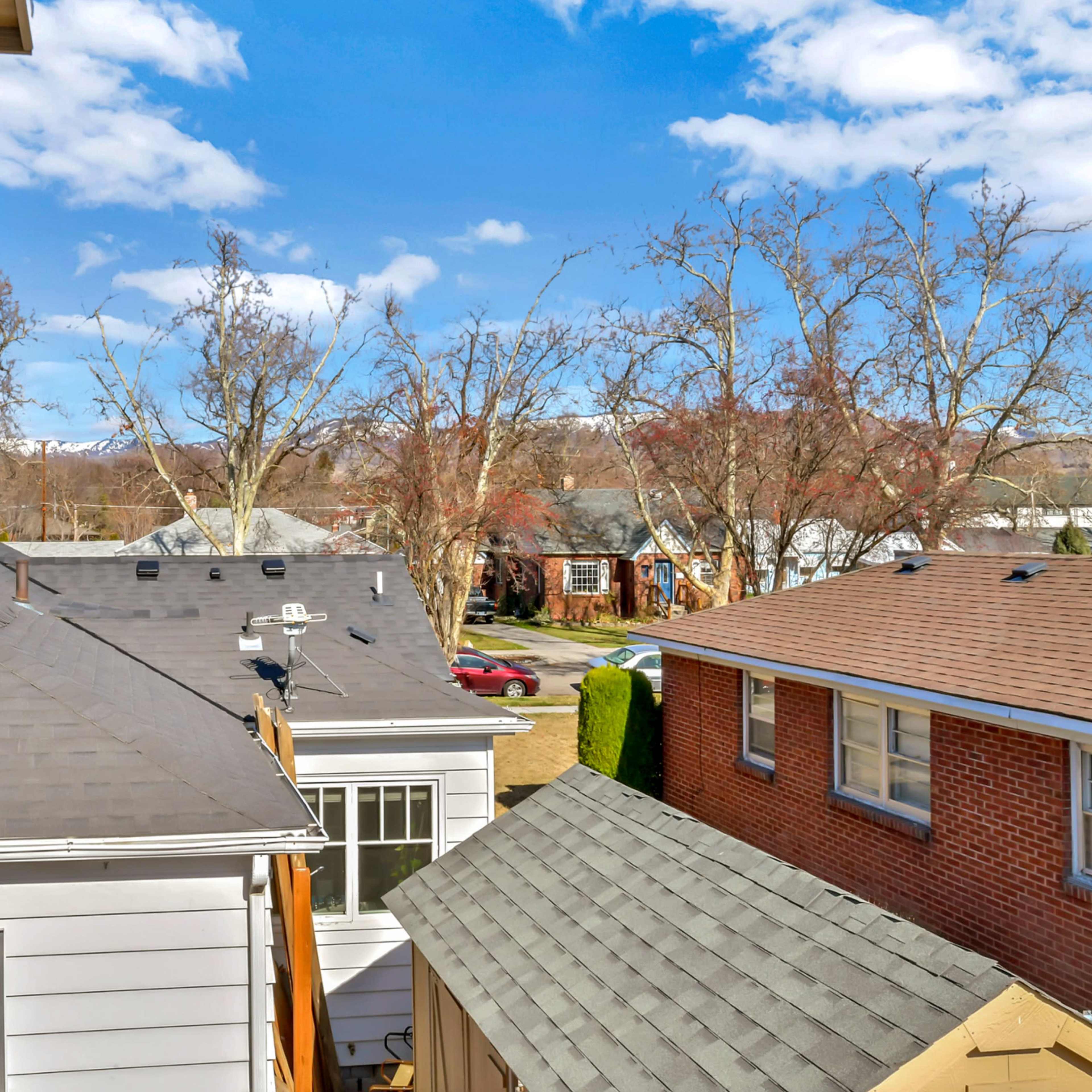 A view of rooftops from a second-story perspective, with trees and houses visible in the background under a blue sky.