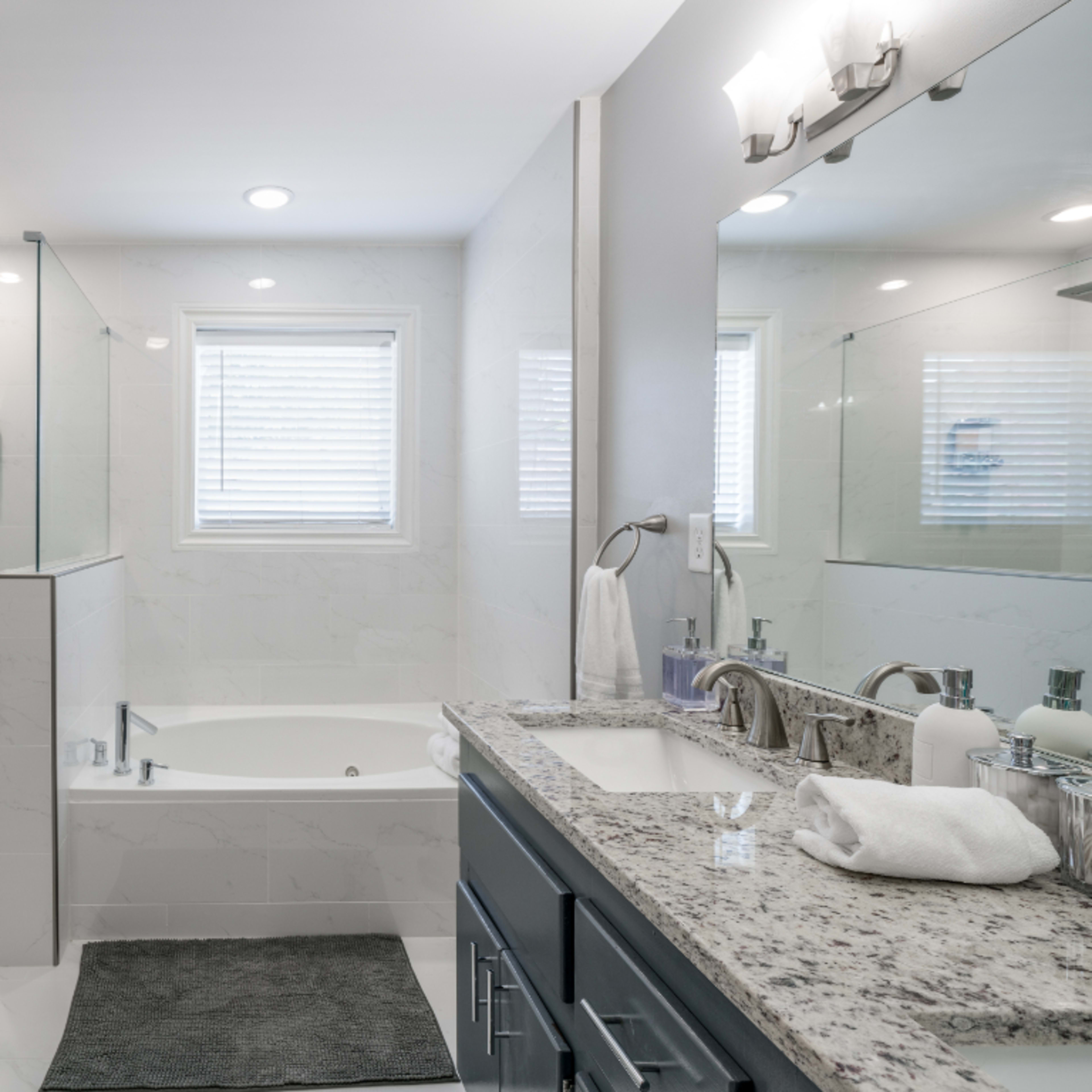 A modern bathroom featuring a glass shower, a freestanding bathtub, a double sink vanity, and neutral-colored tiles.